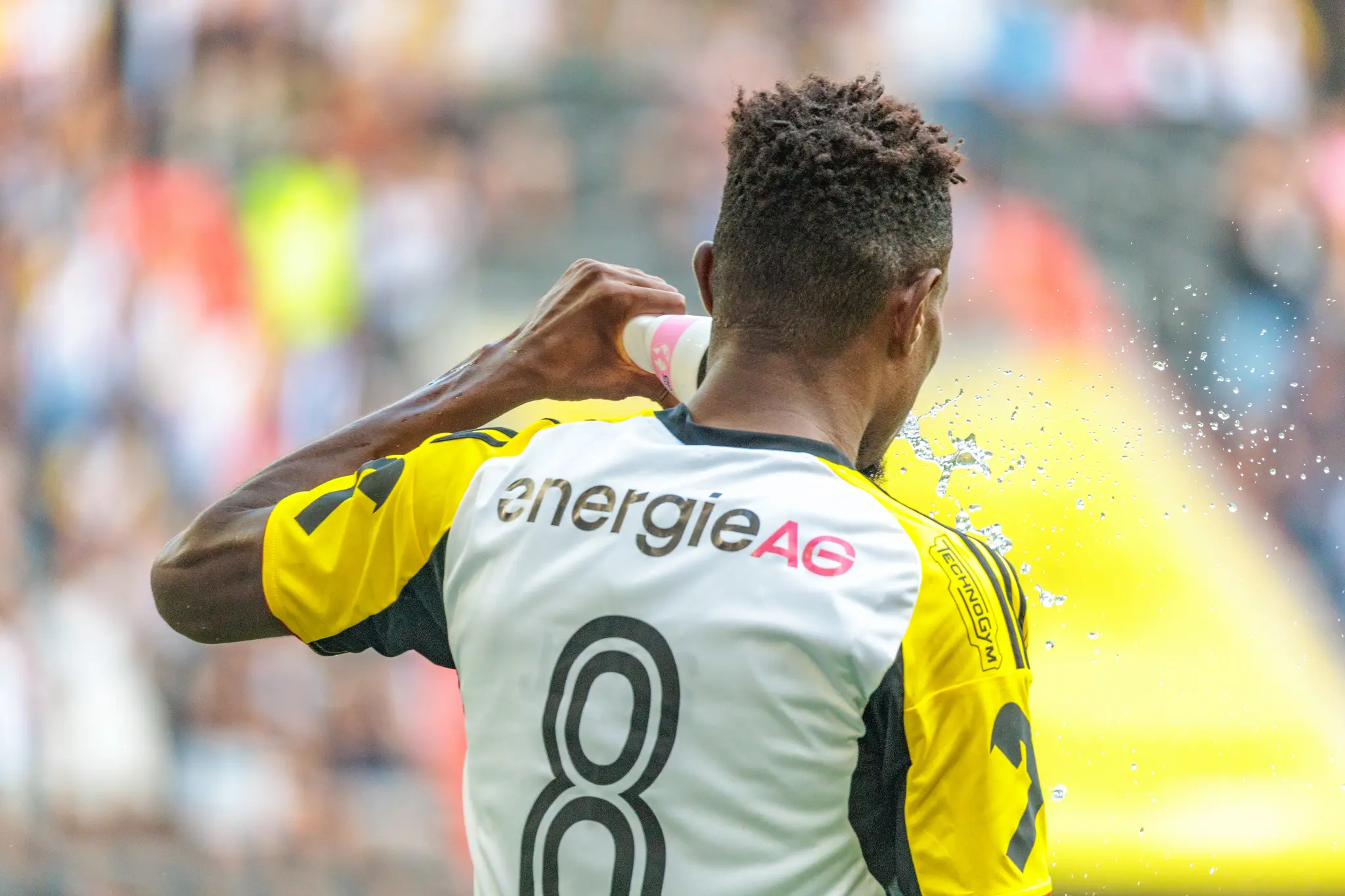 Der LASK-Spieler Moses Usor mit der Rückennummer 8 auf seinem weiß-gelben Trikot erfrischt sich während eines Fußballspiels durch das Spritzen von Wasser aus einer Flasche