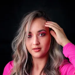 Nahaufnahme einer jungen Frau mit blond-braunem welligem Haar und auffälligem rosa Augen-Make-up, die mit der Hand an der Stirn in die Kamera blickt