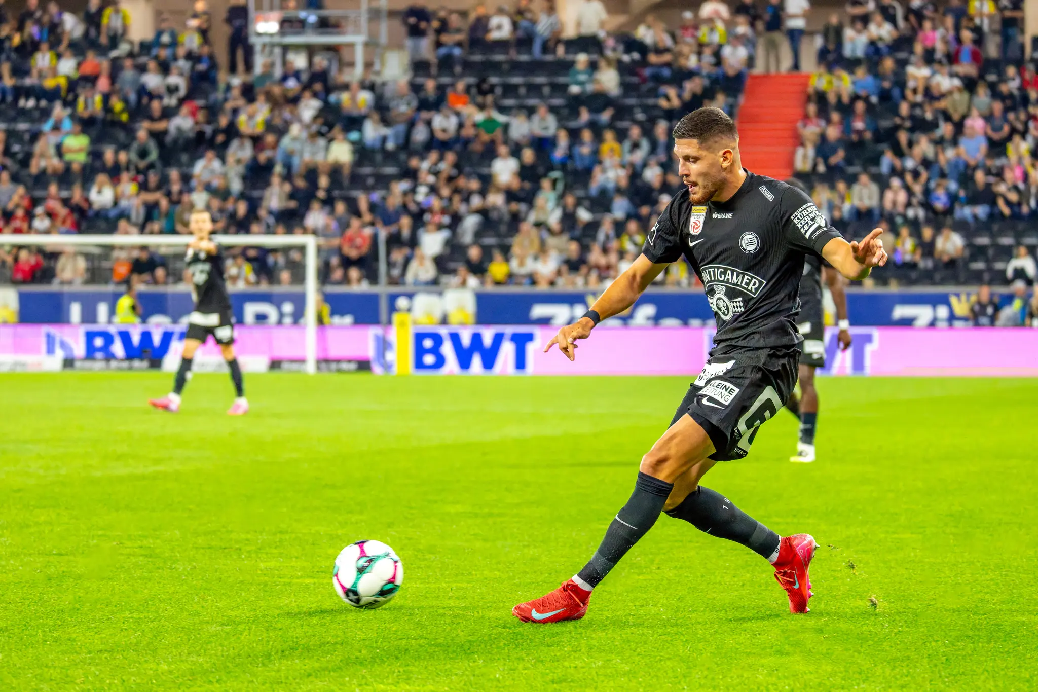 Ein Fußballspieler des SK Sturm Graz in schwarzem Trikot passt den Ball bei einem Bundesligaspiel in der Raiffeisen Arena