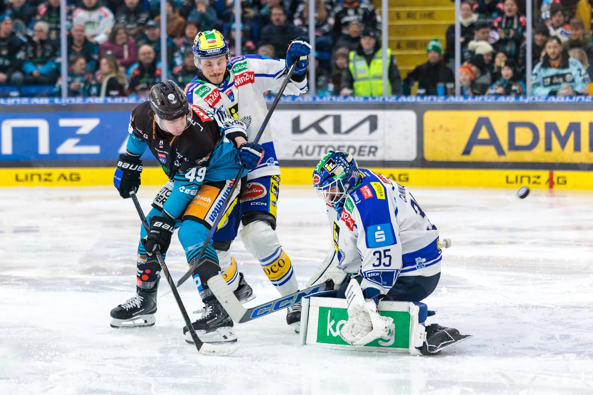 Der VSV-Torhüter (Nummer 35) pariert einen Schuss eines Black Wings Linz-Spielers (Nummer 49) im Eishockey, während der Puck in der Luft schwebt