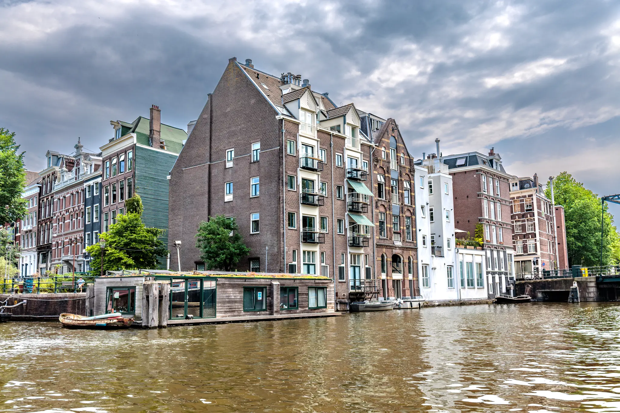 Ein Amsterdamer Kanal gesäumt von schmalen Backsteinhäusern und Hausbooten unter einem bedeckten Himmel 