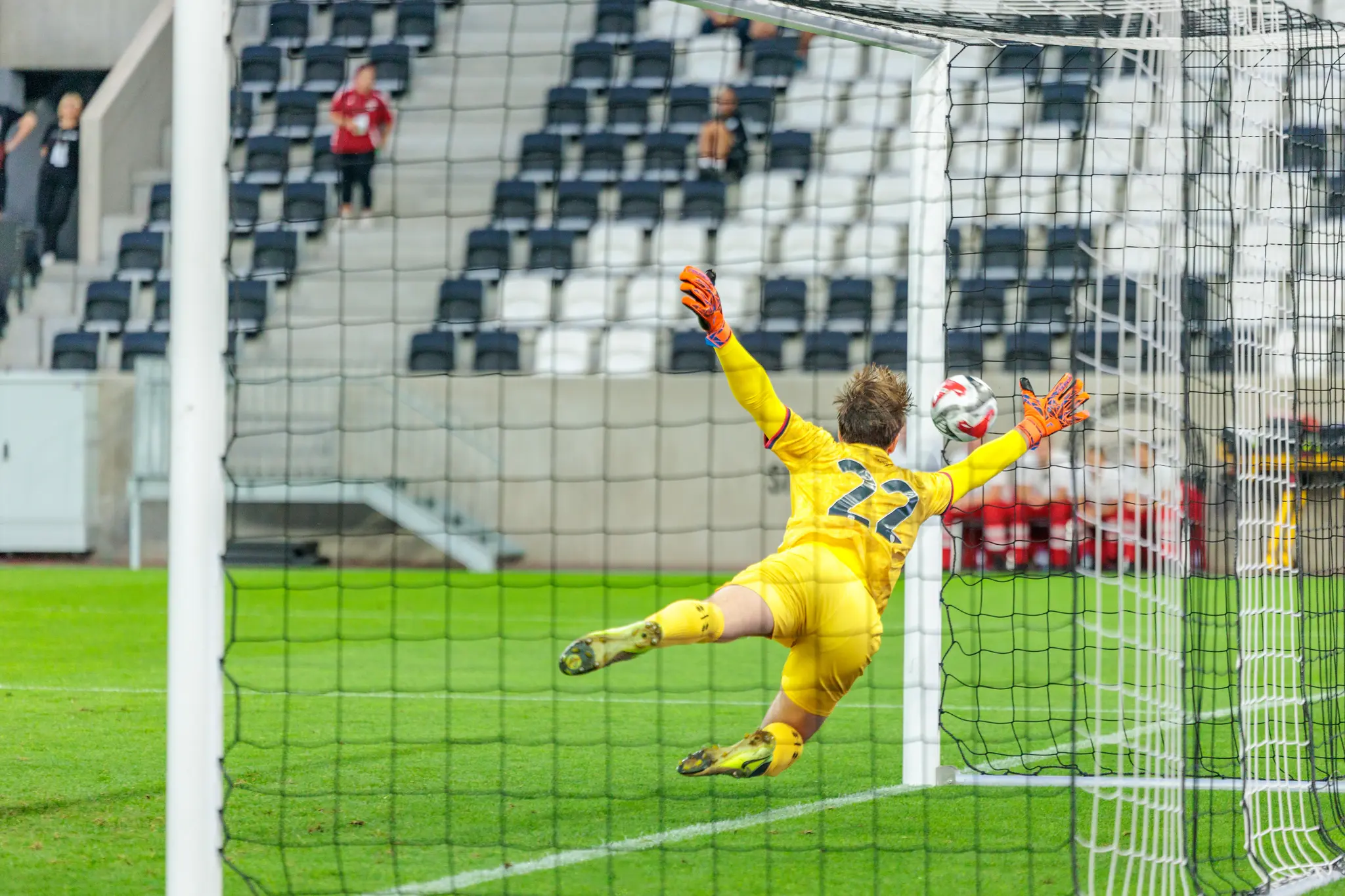 Ein Fußballtorhüter in gelbem Trikot mit der Nummer 22 pariert mit orangefarbenen Handschuhen einen Ball während eines spannenden Spiels der Nero Summer Series 