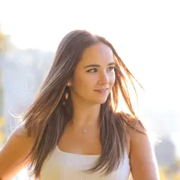 Porträt einer jungen Frau mit windzerzaustem, sonnenbeleuchtetem Haar und einem sanften Lächeln in einer hellen Außenumgebung lens: 56mm F1.4 DC DN | Contemporary 018