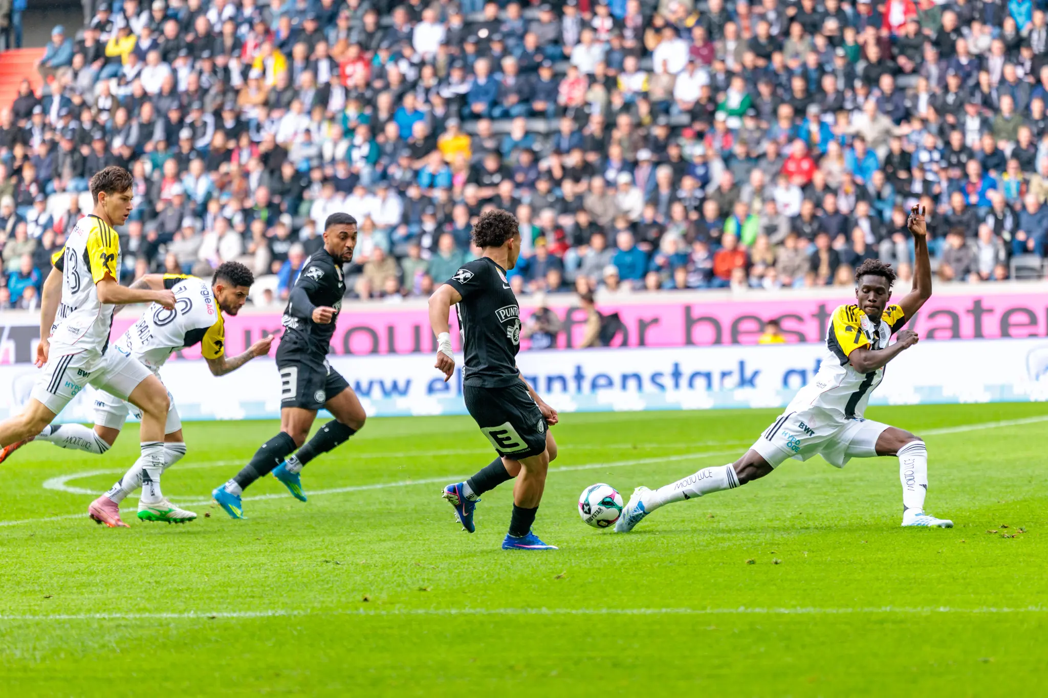 Ein LASK-Spieler streckt sein Bein nach hinten aus um den Pass eines Sturm-Graz-Angreifers zu blockieren