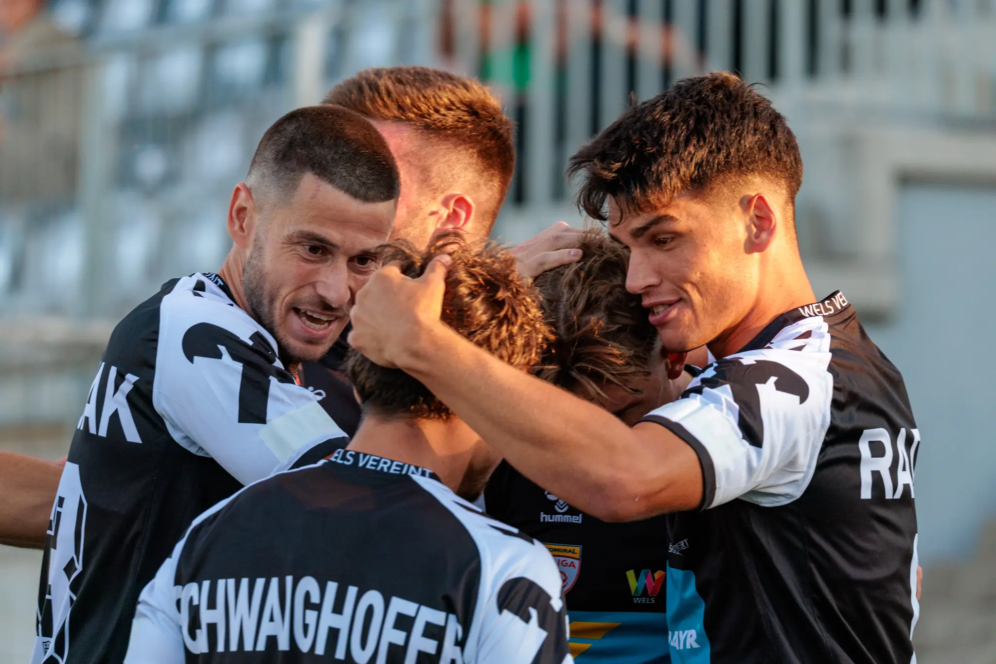 Eng umschlungene Fußballspieler des SPG HOGO Wels teilen freudig ihren emotionalen Torjubel in einem entscheidenden ÖFB-Cup-Spiel