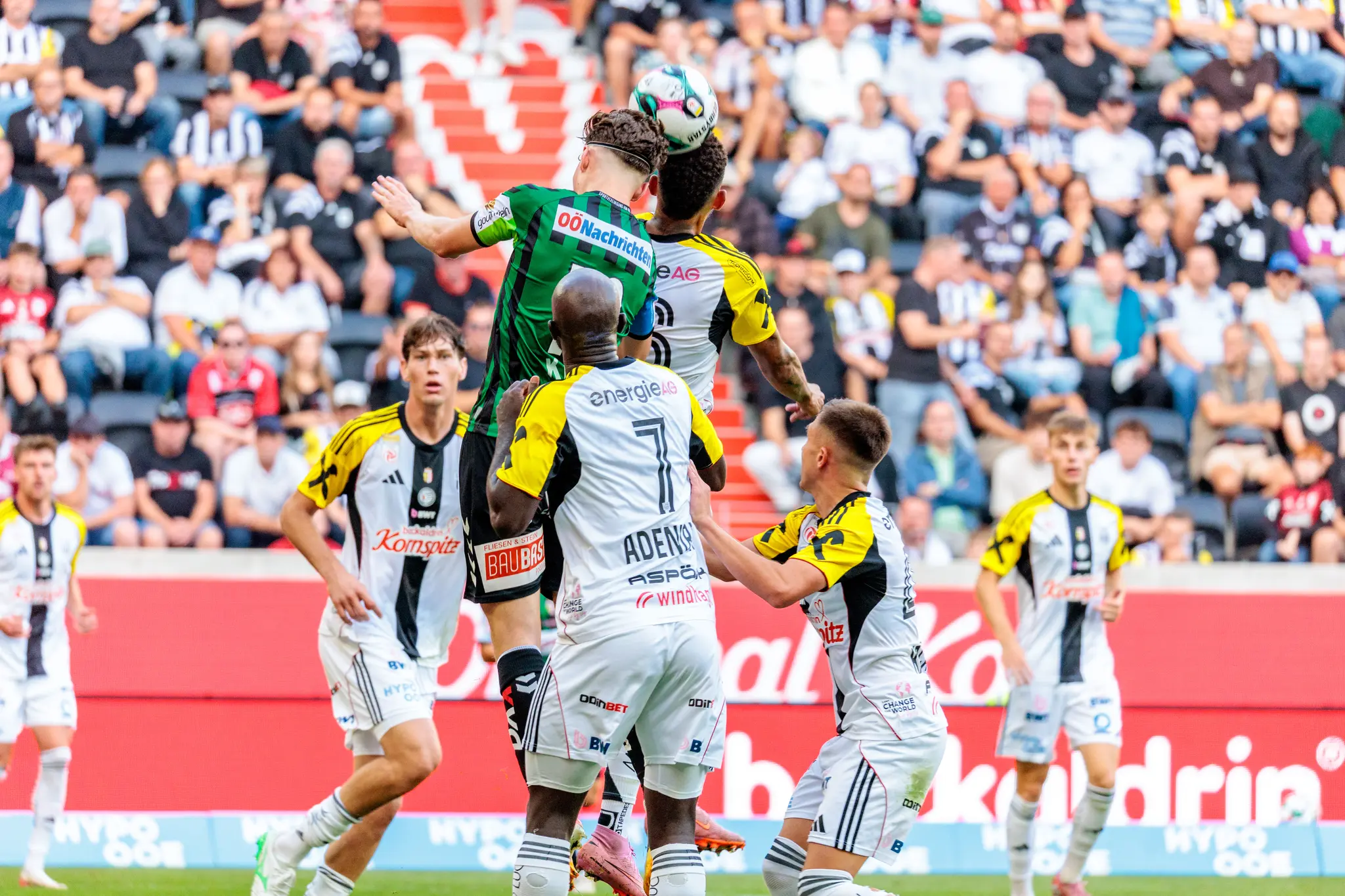 Kopfball-Duell im Strafraum zwischen einem Spieler der SV Ried im grünen Trikot und zwei LASK-Spielern in hellen Trikots während eines Bundesliga-Spiels