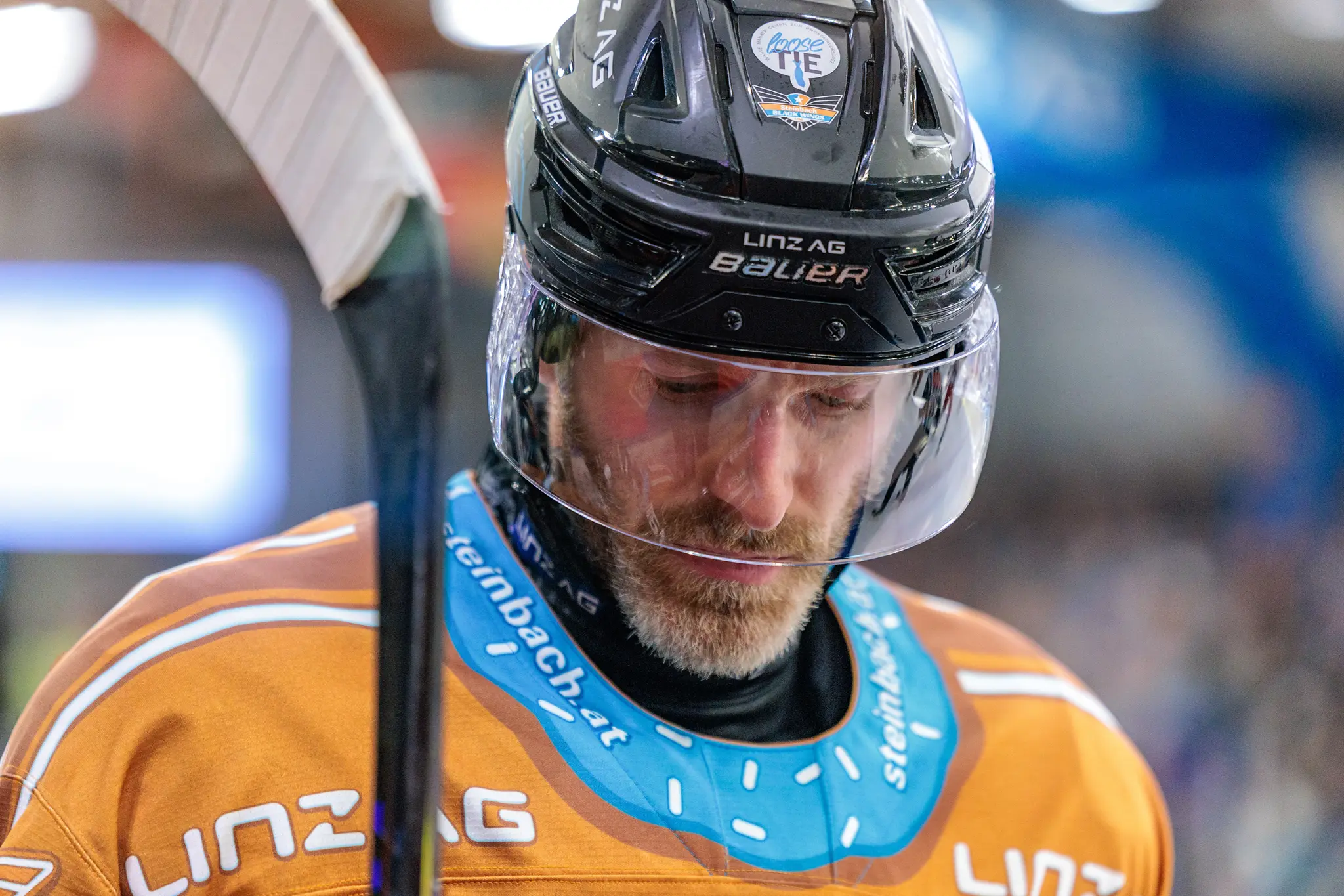 Eishockeyspieler Graham Knott in orangefarbenem Trikot mit Helm und Visier blickt nachdenklich nach unten