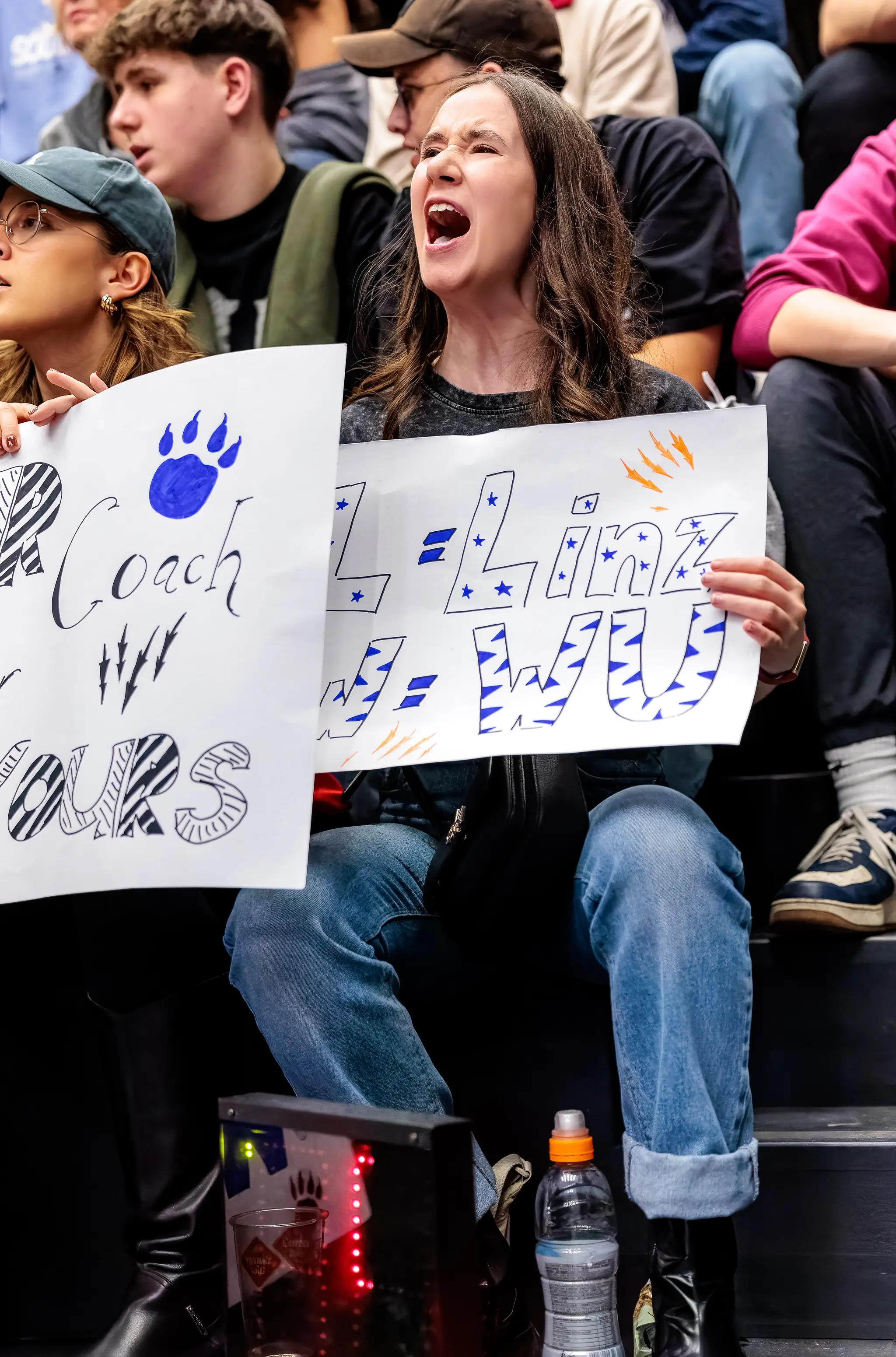 Eine leidenschaftliche Basketball-Anhängerin schreit lautstark und hält zwei selbstgemachte Fan-Plakate hoch 