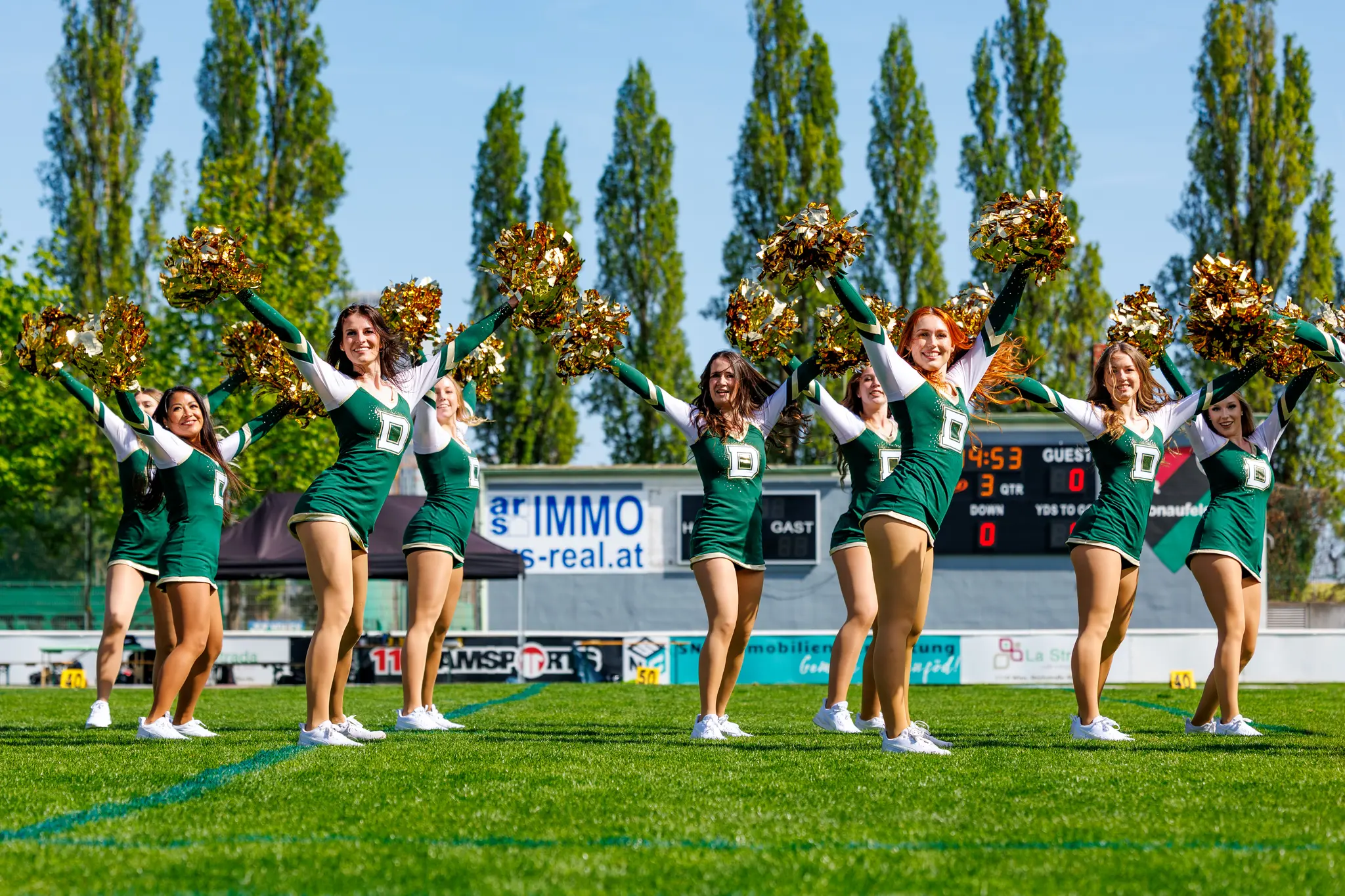 Die Premium Dancers der Danube Dragons posieren mit erhobenen goldenen Pompoms und jubeln in ihren grün-weißen Uniformen bei einem Spiel der Austrian Football League