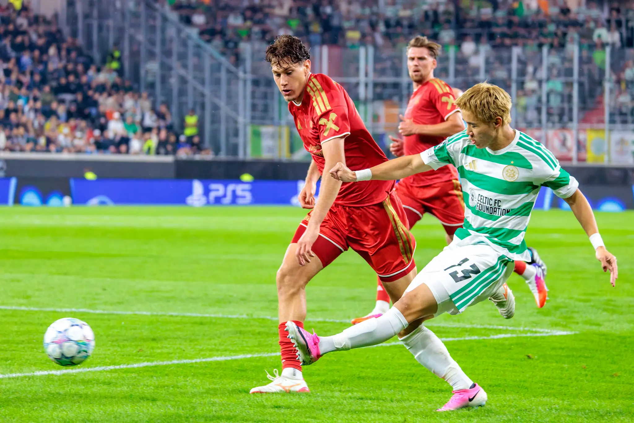 Celtic-Stürmer Yang (13) schiebt den Ball mit links nach vorn, während zwei LASK-Verteidiger in Rot eng dran bleiben und zum Zweikampf ansetzen.