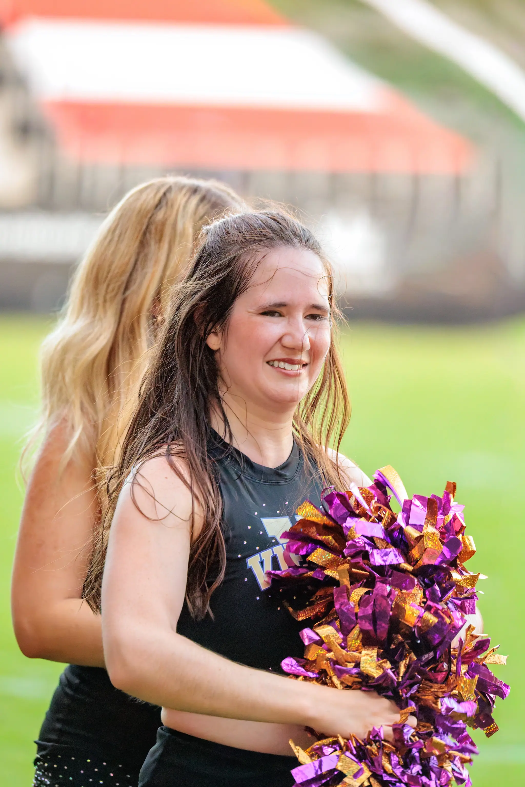 Junge Tänzerin des Vienna Vikings Cheer Squads lächelt in die Kamera, den Arm voll lila-goldener Pompons.