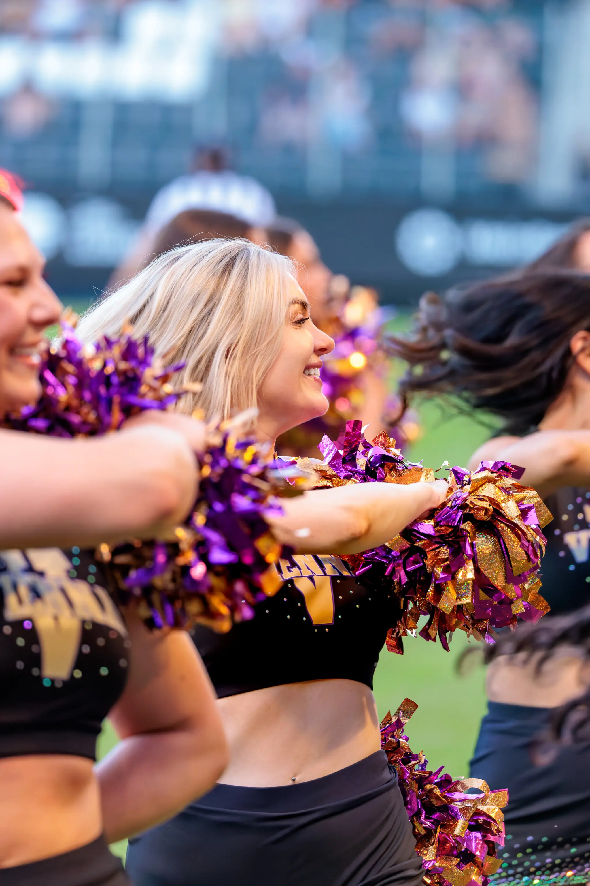 Cheerleaderin des Spirit Squad streckt die Arme mit violett-goldenen Pompons in einer Tanzbewegung.