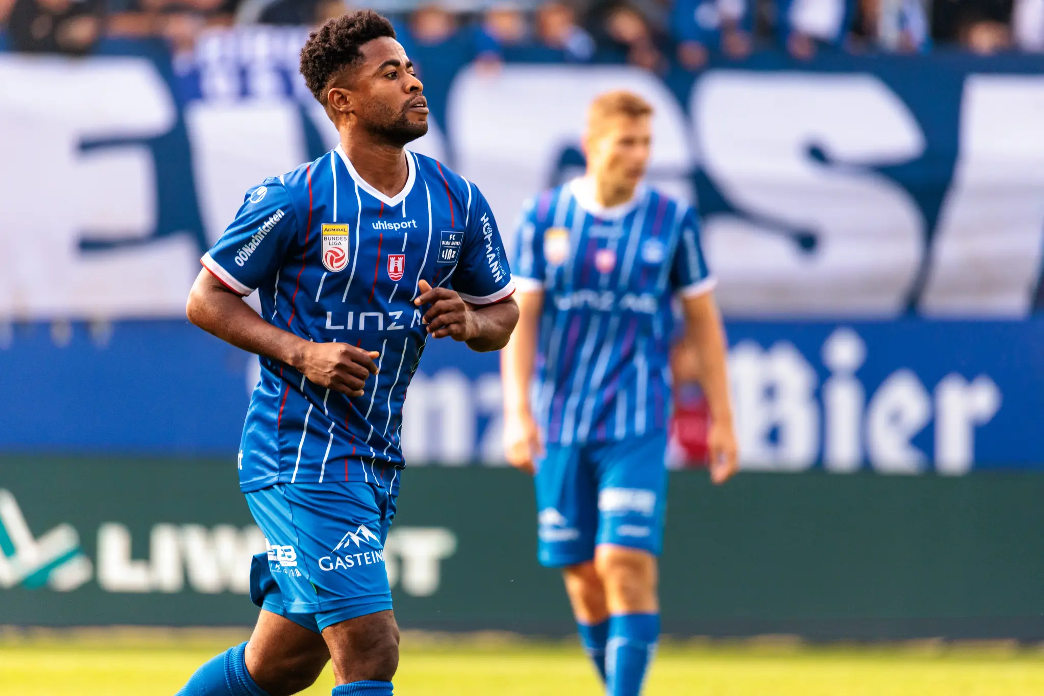 Ein dunkelhäutiger Fußballspieler des FC Blau-Weiß Linz mit Bart läuft im blau-weiß gestreiften Trikot konzentriert während eines Bundesligaspiels