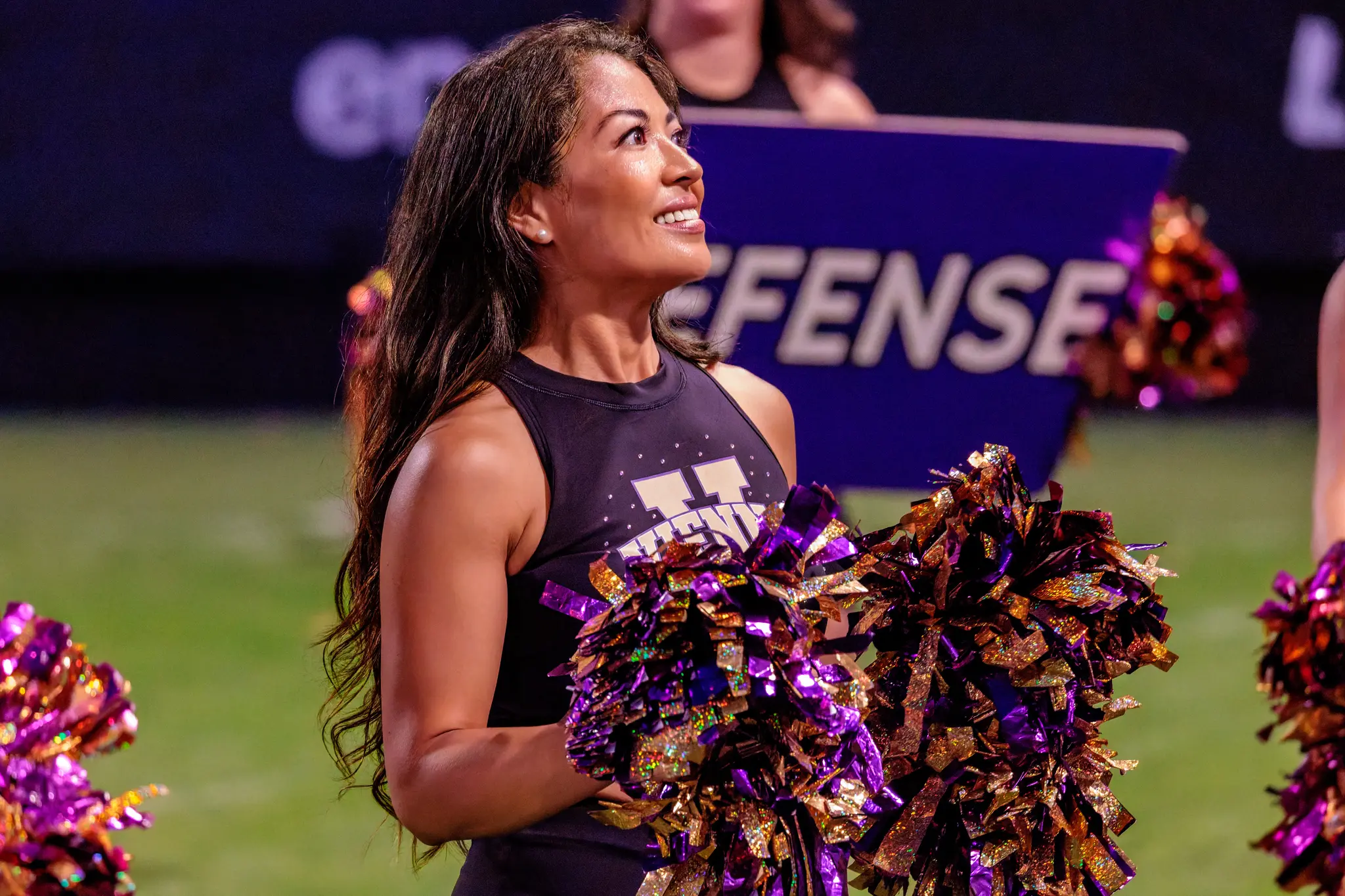 Blick nach oben, Pompons in Violett-Gold: Eine Tänzerin des Vienna Vikings Spirit Squad fiebert dem nächsten Play entgegen, hinter ihr leuchtet das „DEFENSE“-Schild – bereit für den nächsten Spielzug gegen die Red Lions.
