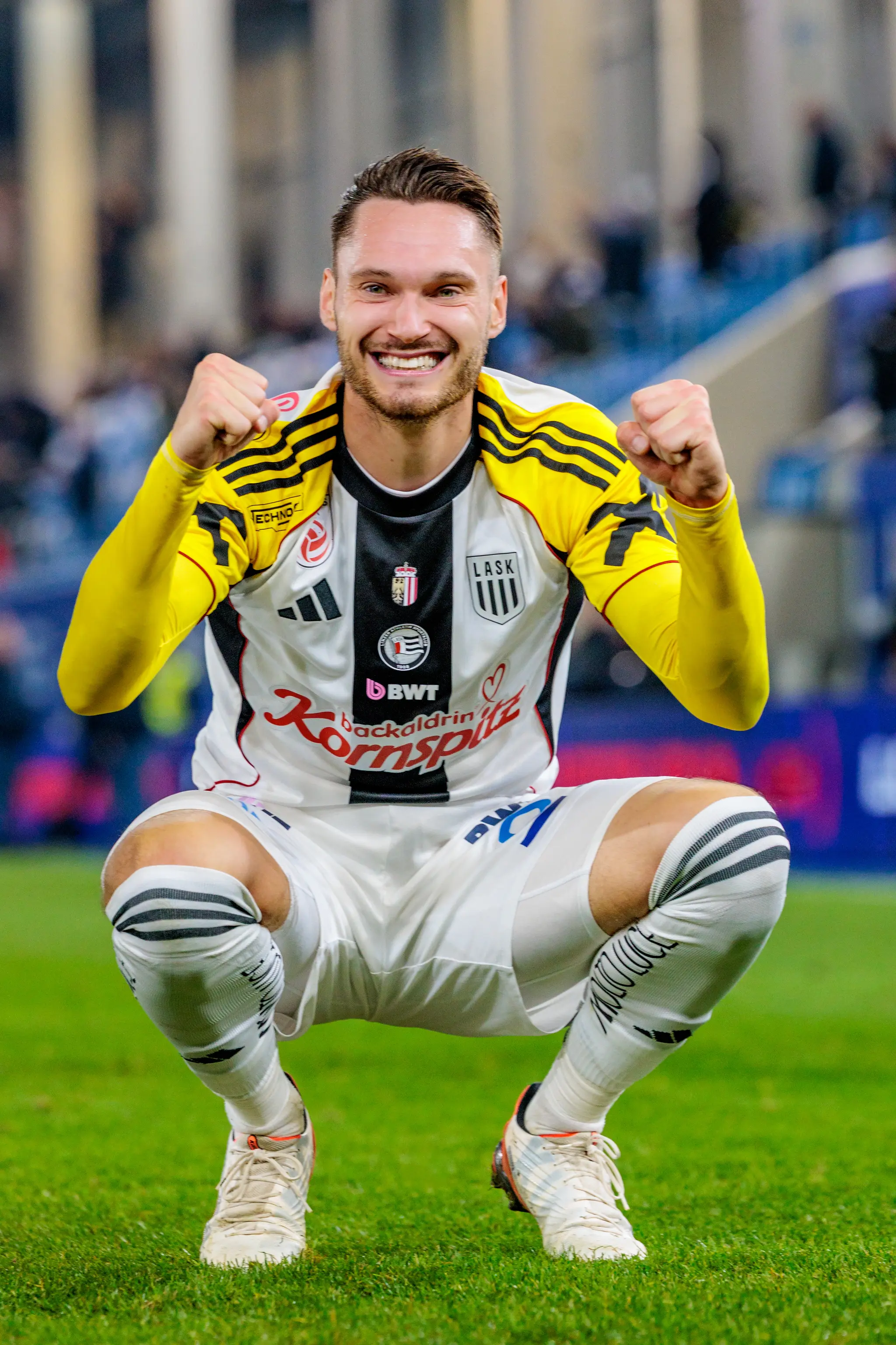 Der LASK-Spieler Valon Berisha geht in die Hocke, lächelt breit in die Kamera und ballt jubelnd seine Fäuste nach dem Spiel