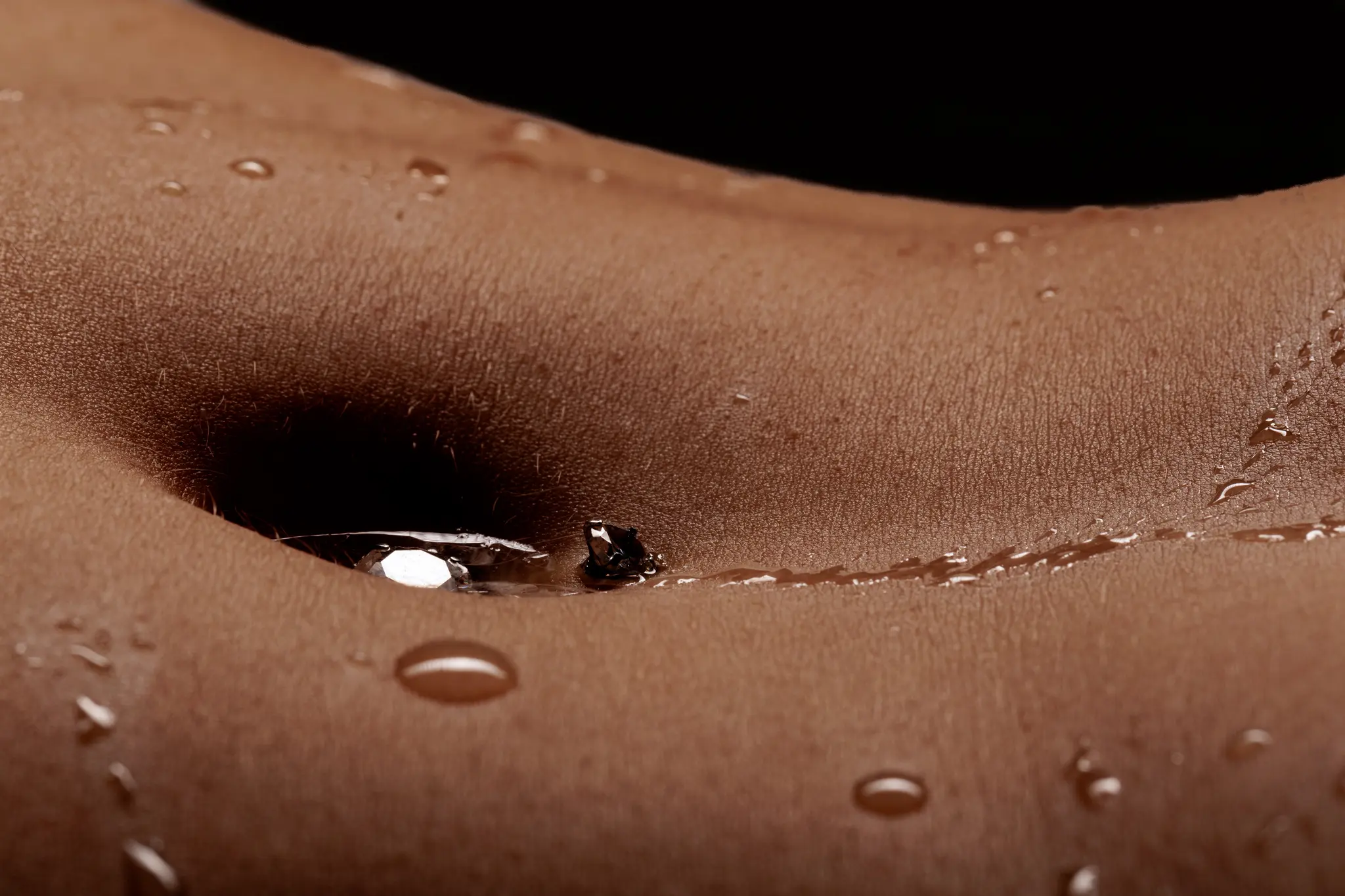 Eine ästhetische Nahaufnahme menschlicher Haut, die mit glitzernden Wassertropfen bedeckt ist und den Bauchnabel zeigt 