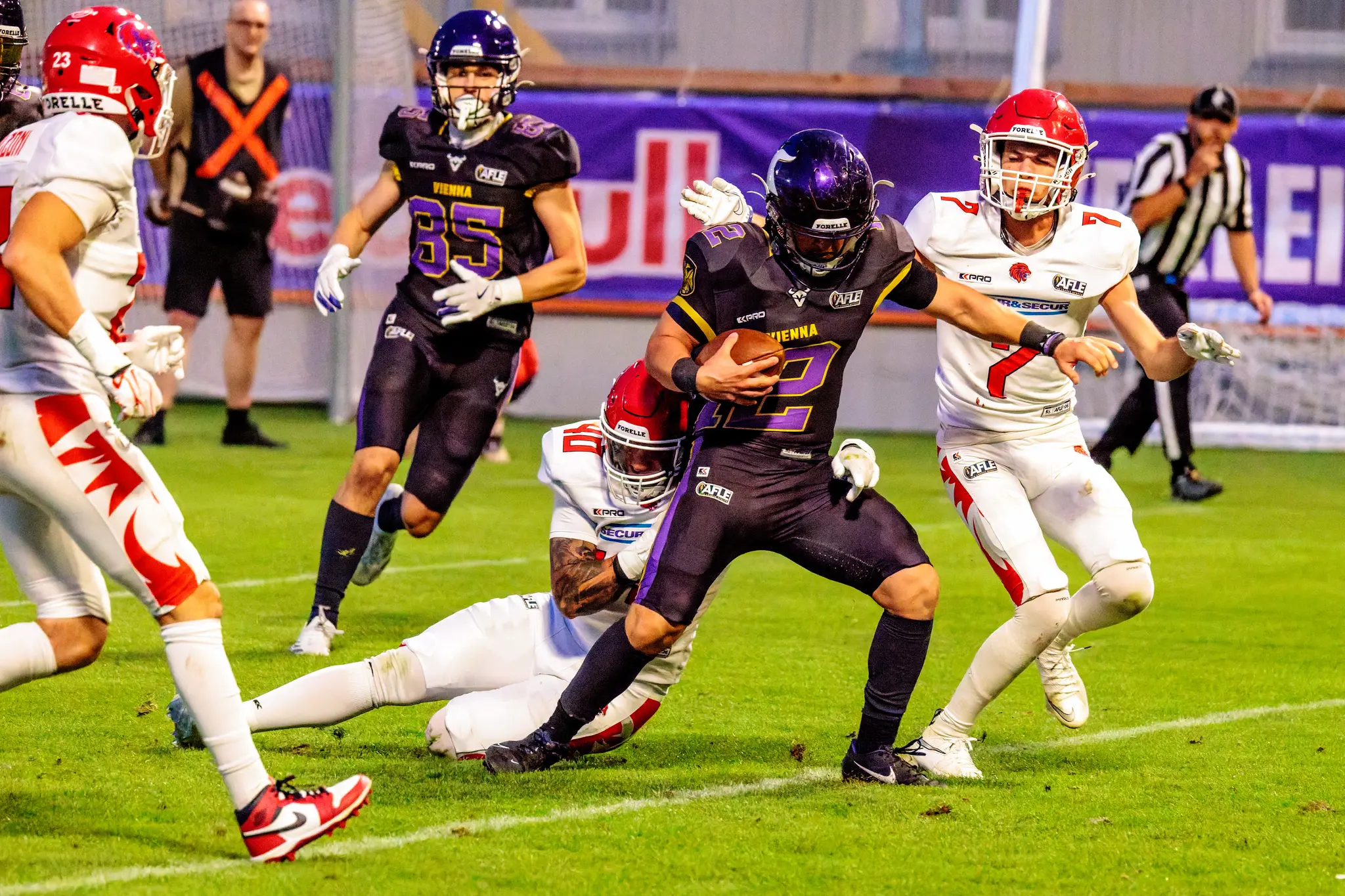 Nico Hrouda (12) windet sich mit dem Ball unterm Arm aus dem Tackle-Griff eines Red-Lions-Verteidigers, während Gäste-Nummer 7 nachsetzt.