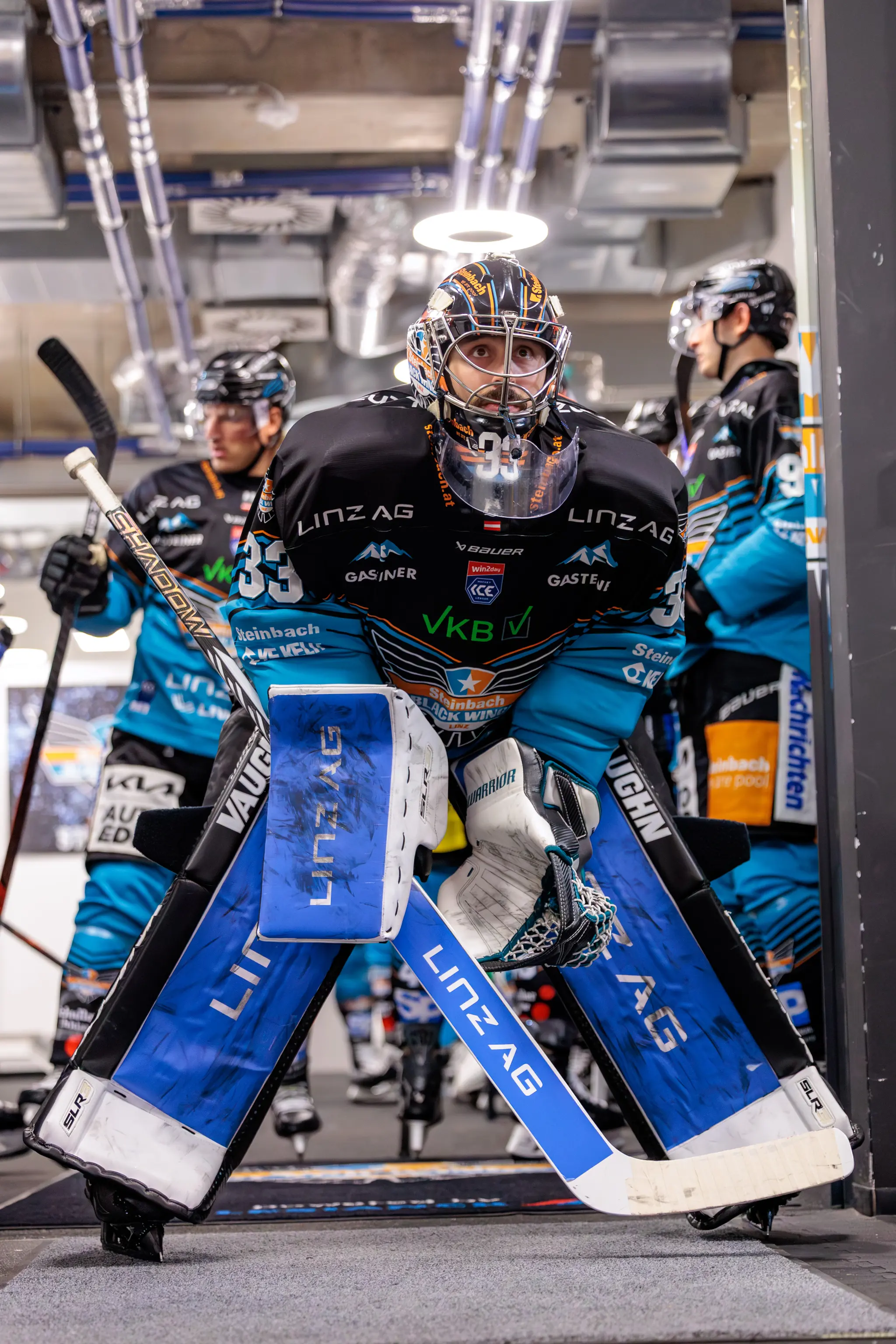 Der Eishockey-Goalie Thomas Höneckl von den Steinbach Black Wings Linz blickt in voller Montur und mit einem leuchtenden Ring über dem Helm konzentriert aus dem Spielertunnel