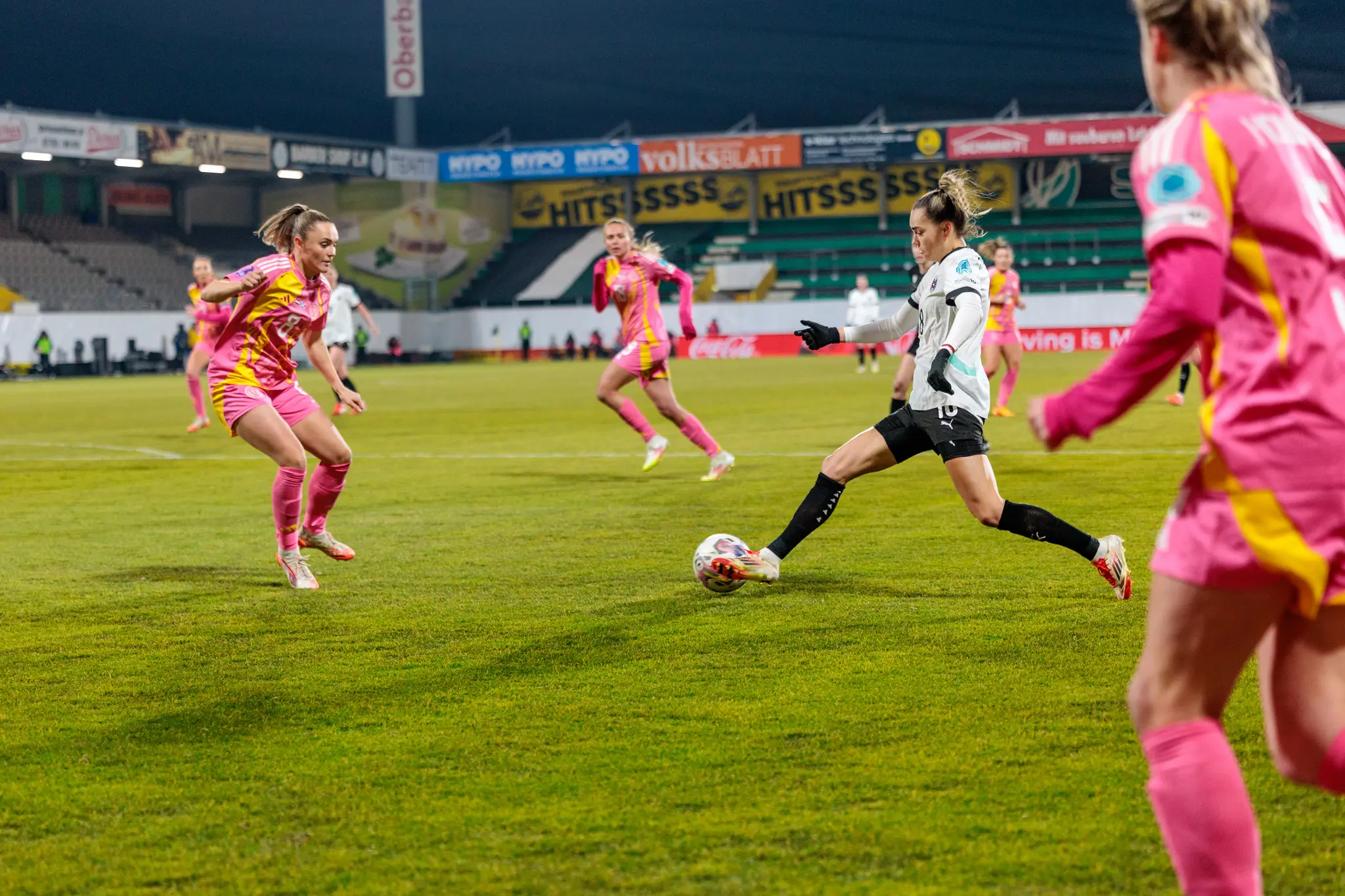 Eine österreichische Fußballspielerin in weißem Trikot tritt den Ball während eines Damenfußballspiels im Stadion unter Flutlicht 