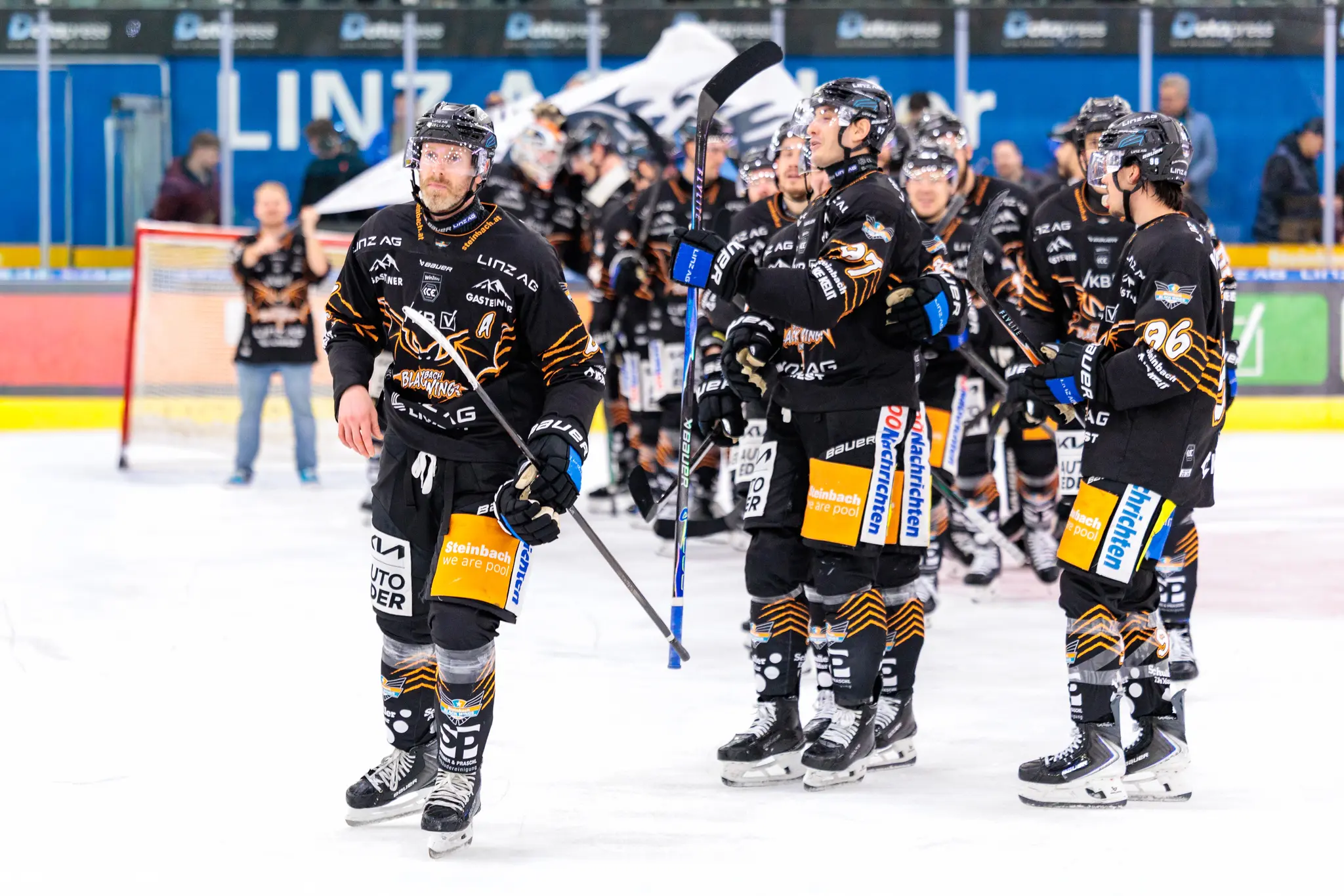 Der Eishockeyprofi Brian Lebler von den Black Wings Linz steht mit seinem Schläger auf dem Eis, umgeben von Teamkollegen in schwarzen Trikots