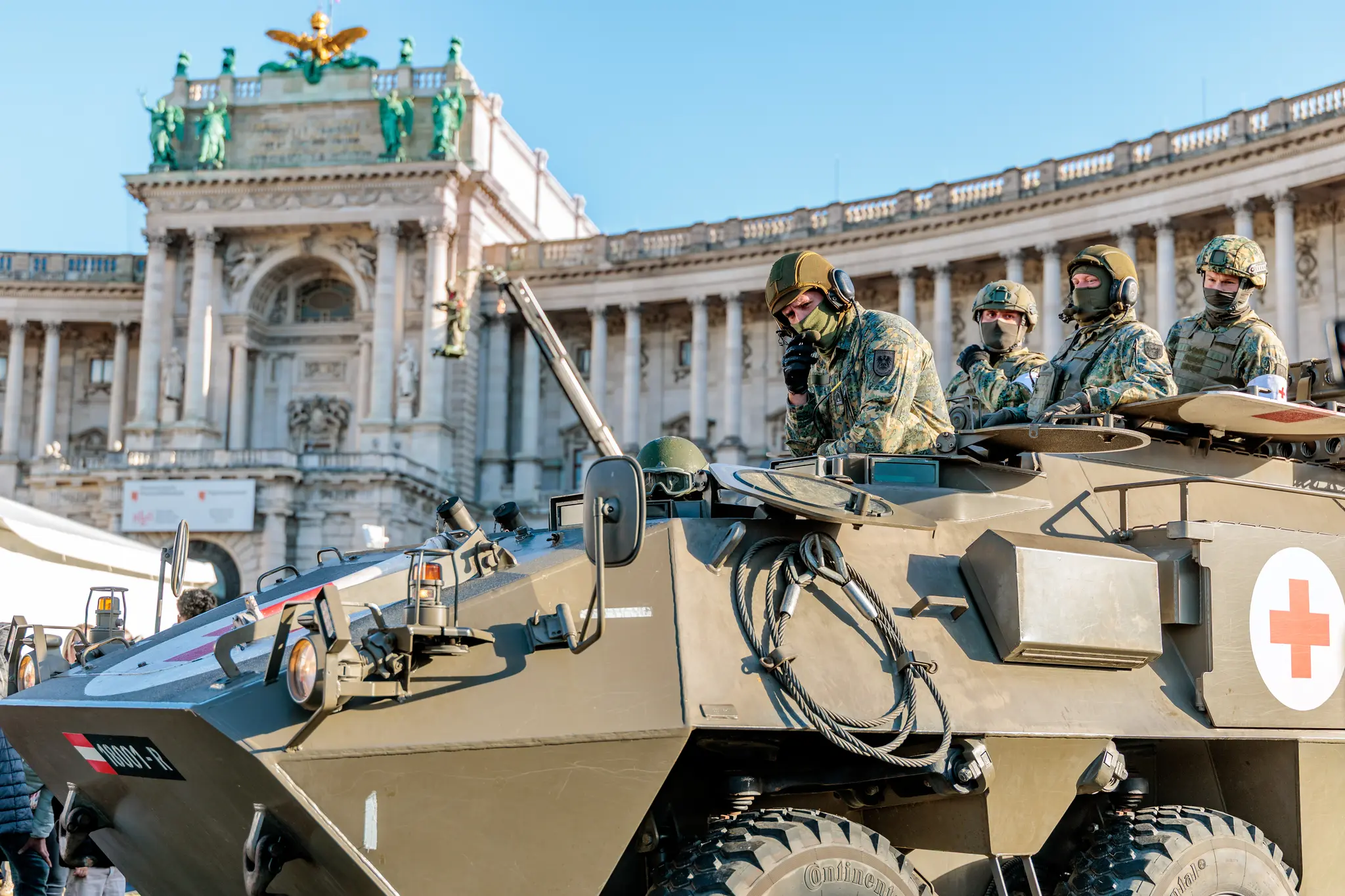 Ein Sanitätspanzer Pandur (6x6) des österreichischen Bundesheeres rollt vor der Neuen Burg, oben stehen Soldaten in Tarnuniform.