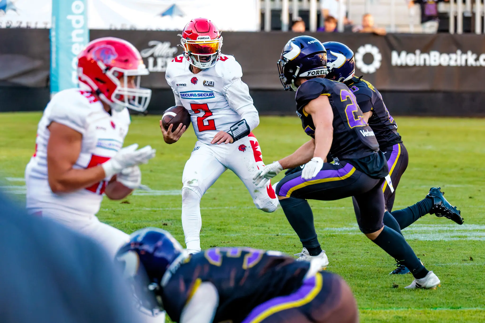 Fluchtversuch unter Druck: Der Red-Lions-Ballträger (2) mit verspiegeltem Visor versucht auszubrechen, während die Vikings-Defender die Zange schließen.