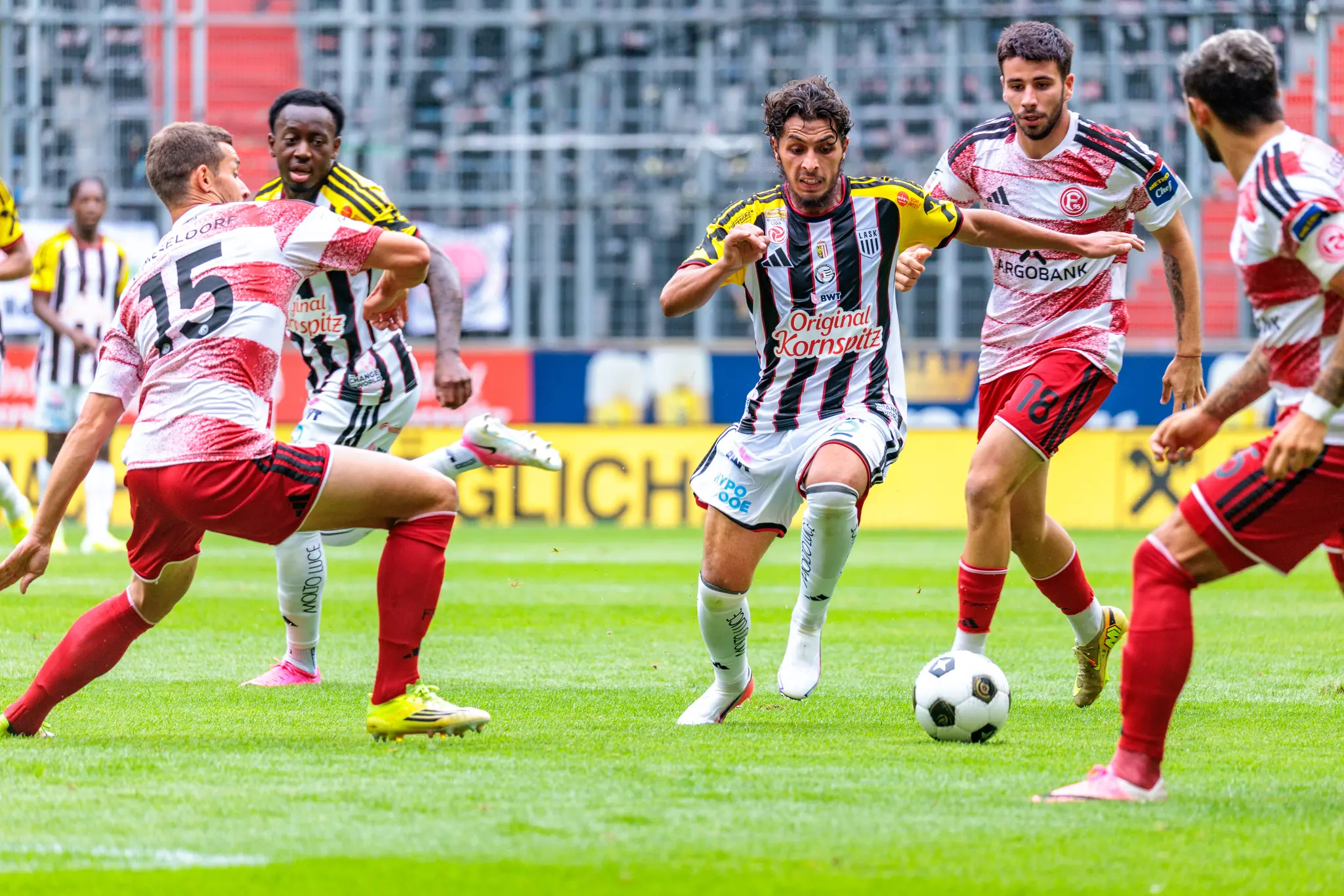 LASK-Spieler dribbelt mit dem Ball am Fuß durch drei Düsseldorfer Verteidiger, intensive Kampfszene mit mehreren Spielern um den Ball herum.