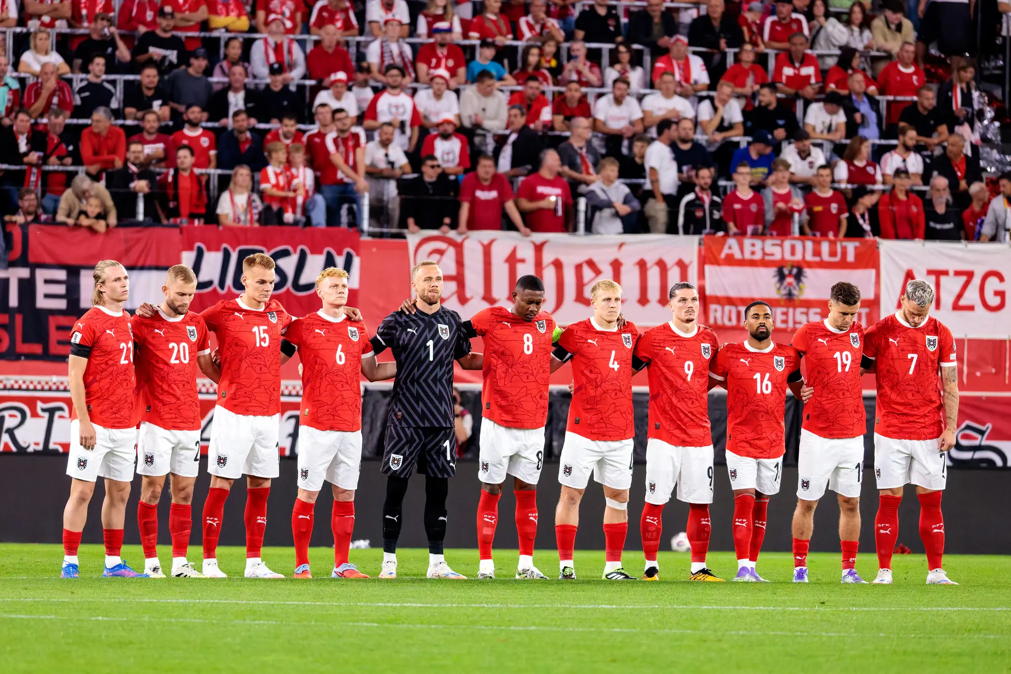 Die österreichische Fußballnationalmannschaft steht in roten Trikots eng zusammen auf dem Spielfeld und hält eine Schweigeminute ab