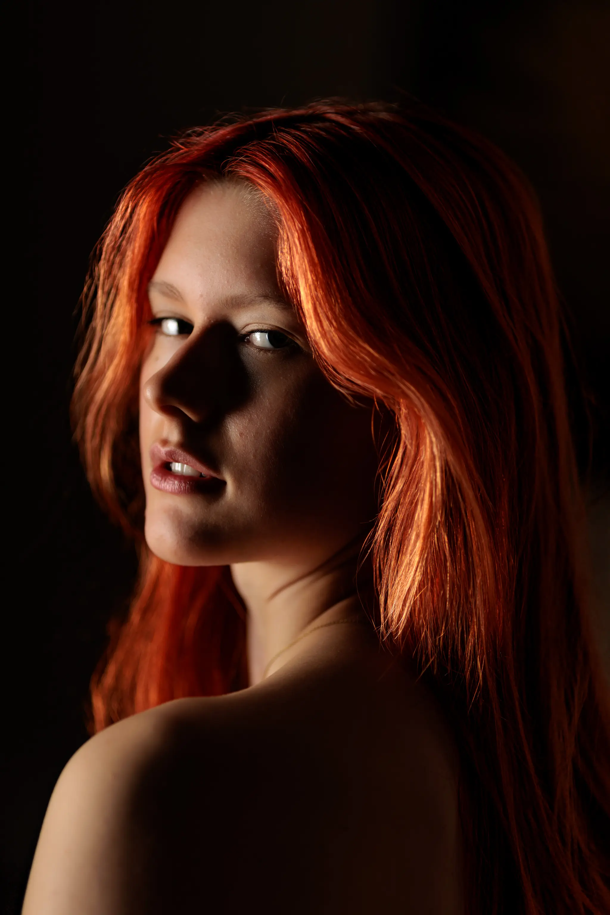 Ein sinnliches Porträt von Sarah mit leuchtend roten Haaren, die sich über die Schulter dreht und dabei von einem warmen Streiflicht umspielt wird