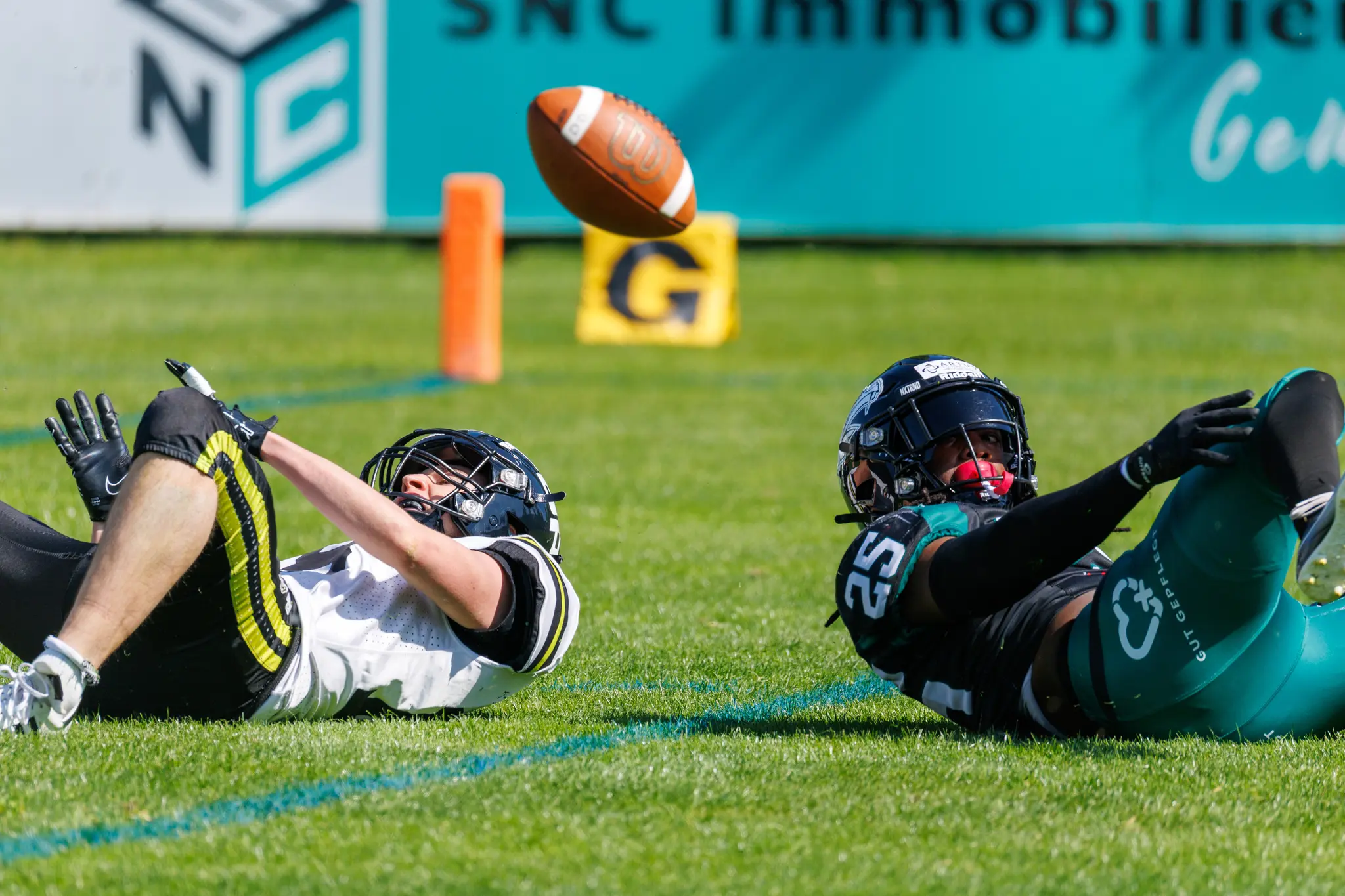 Ein American Football schwebt in der Luft über zwei am Boden liegenden Spielern der Danube Dragons und Prague Black Panthers während eines Spiels der Austrian Football League