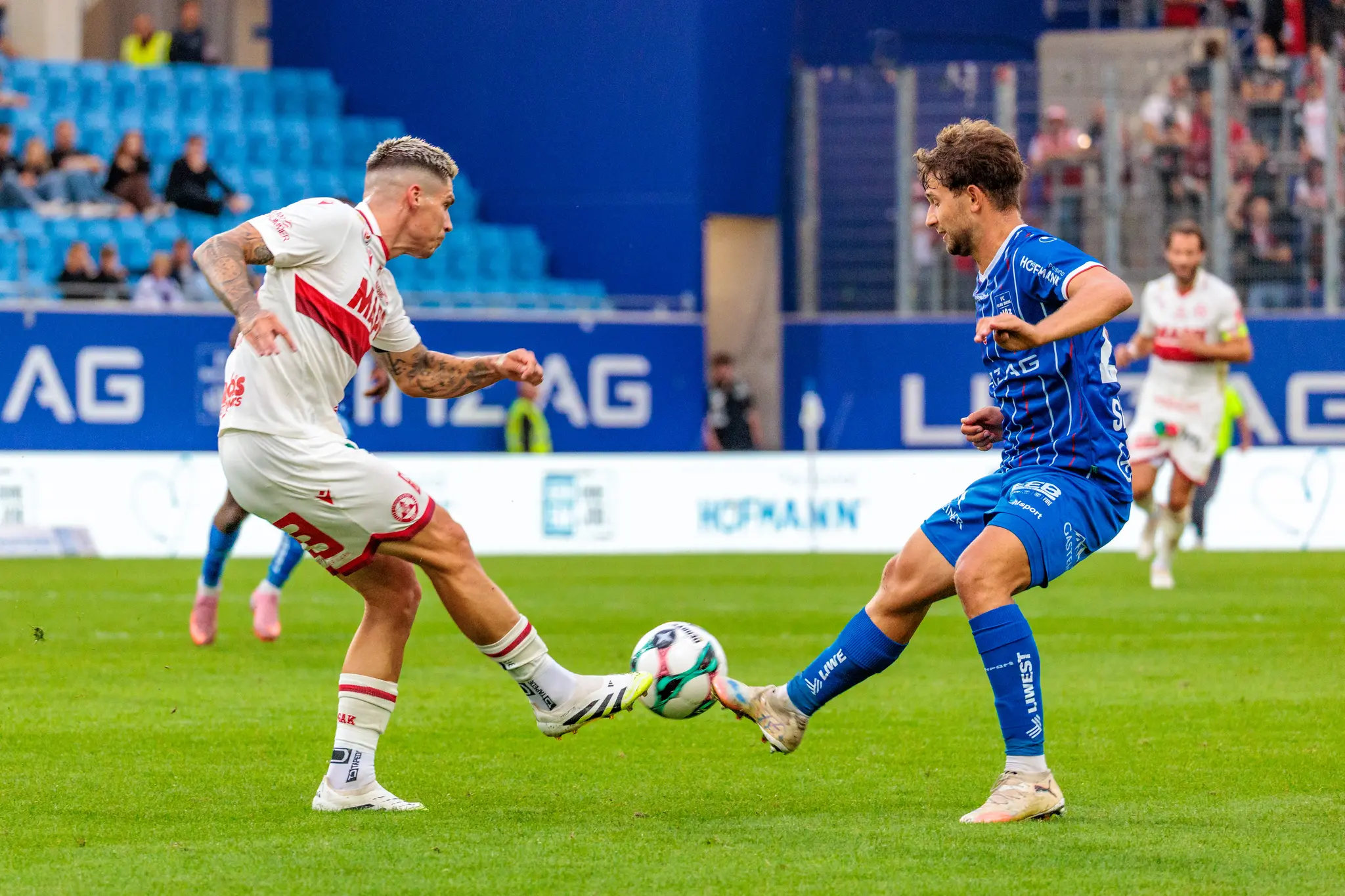 Zwei Fußballspieler, Alexander Briedl von Blau-Weiß Linz in blauem Trikot und Tio Cipot vom GAK in weißem Trikot, kämpfen während eines Ligaspiels um den Ball