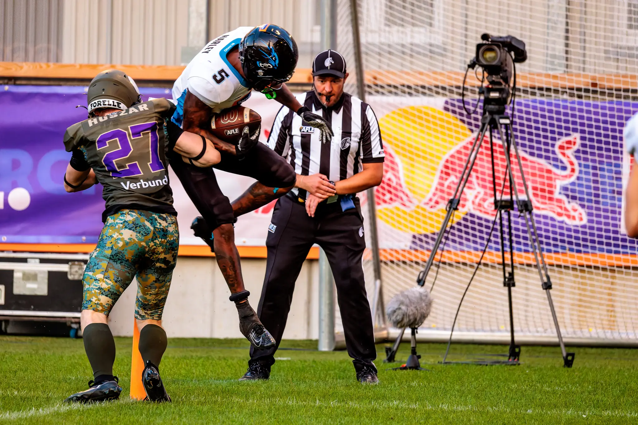Panthers-Spieler Nummer 5 springt in hoher Laufbewegung an der Goalline in die Endzone, Vikings Nummer 27 (Nikolaus Huszar) versucht ihn zu stoppen.