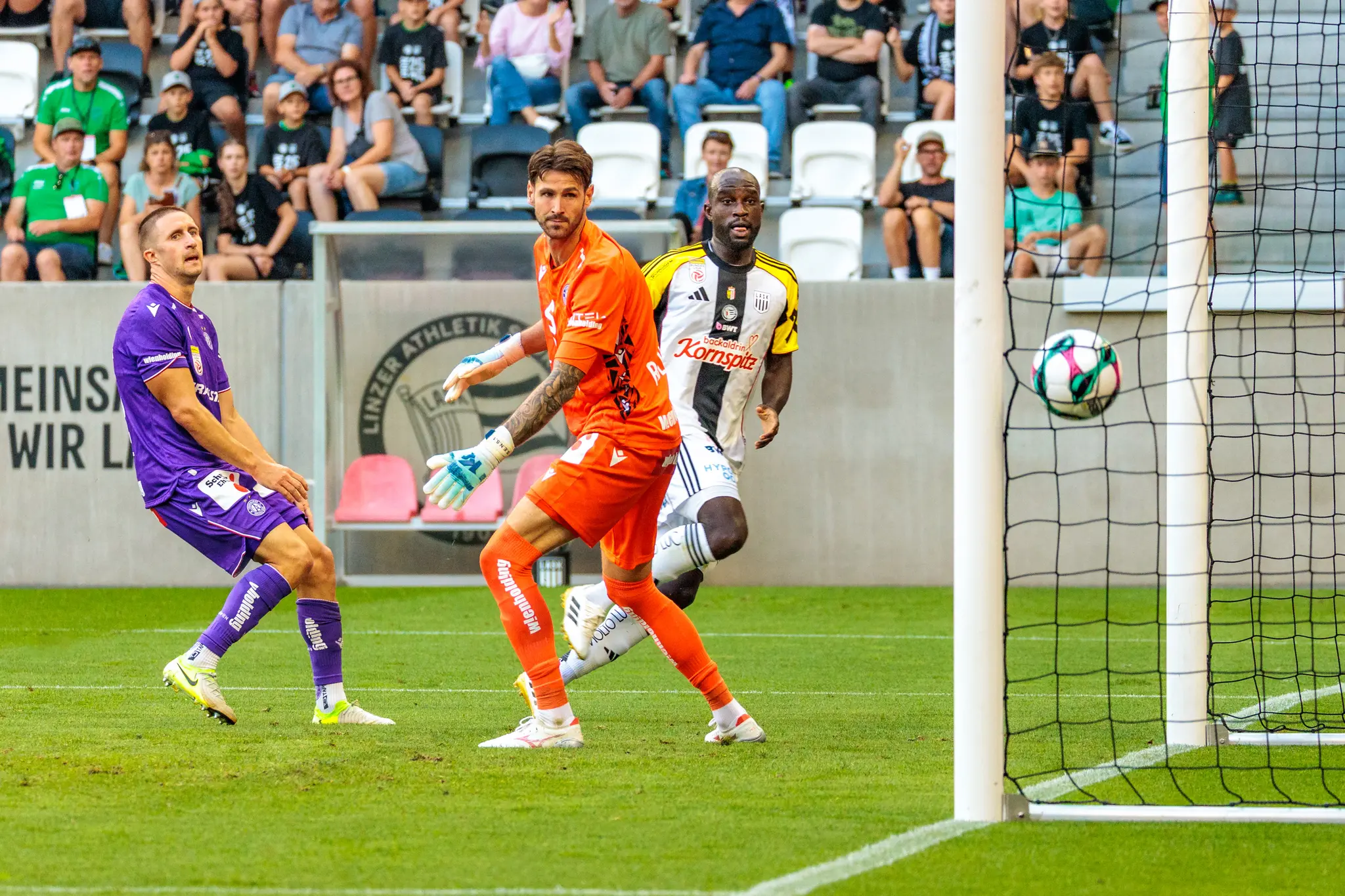 Der Ball liegt im Tornetz, während Fußballspieler des LASK und von Austria Wien auf das soeben erzielte Tor blicken