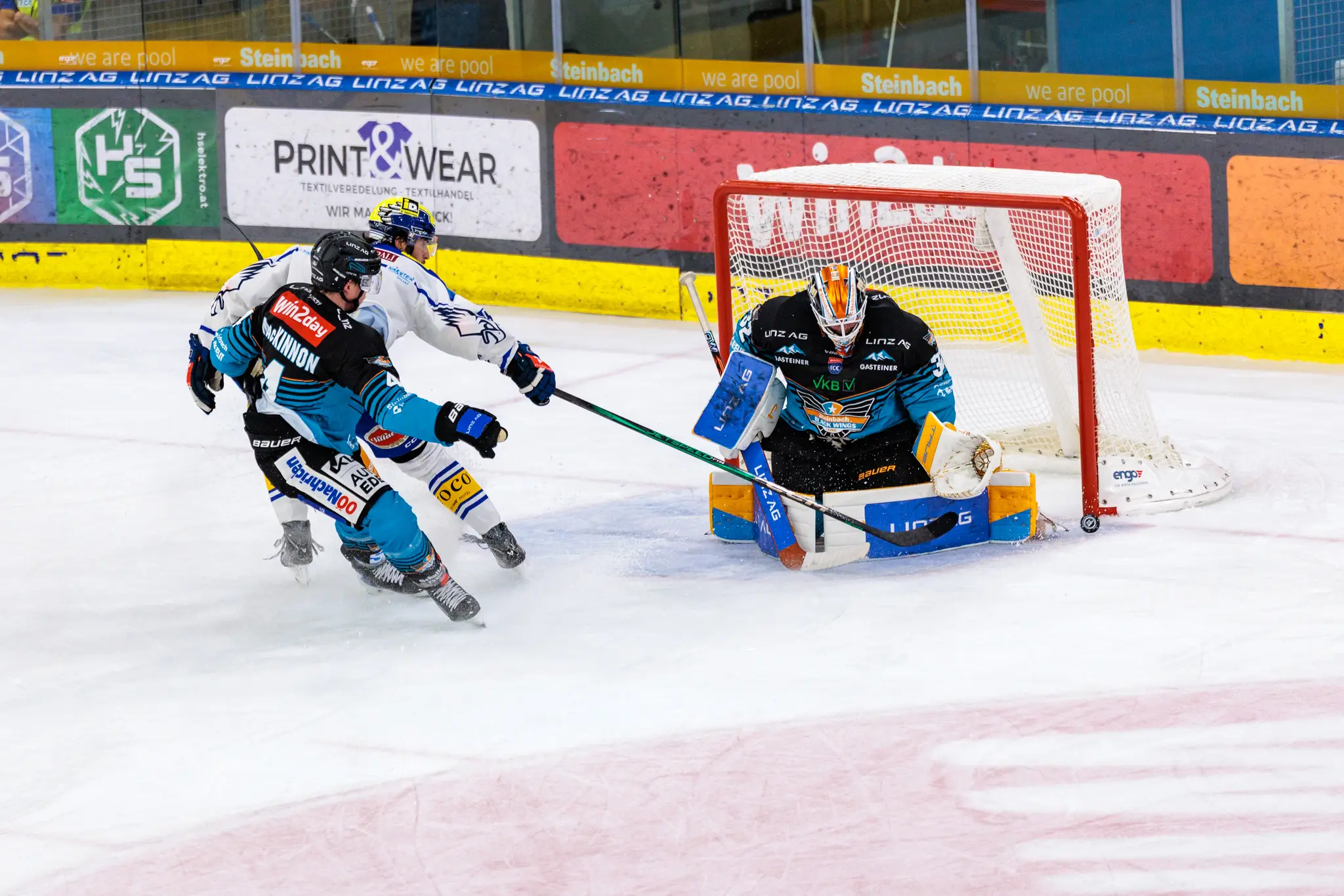 Eishockey-Torhüter Rasmus Tirronen von den Steinbach Black Wings Linz pariert einen Schuss, während Ryan MacKinnon und Adam Helewka vor dem Tor agieren