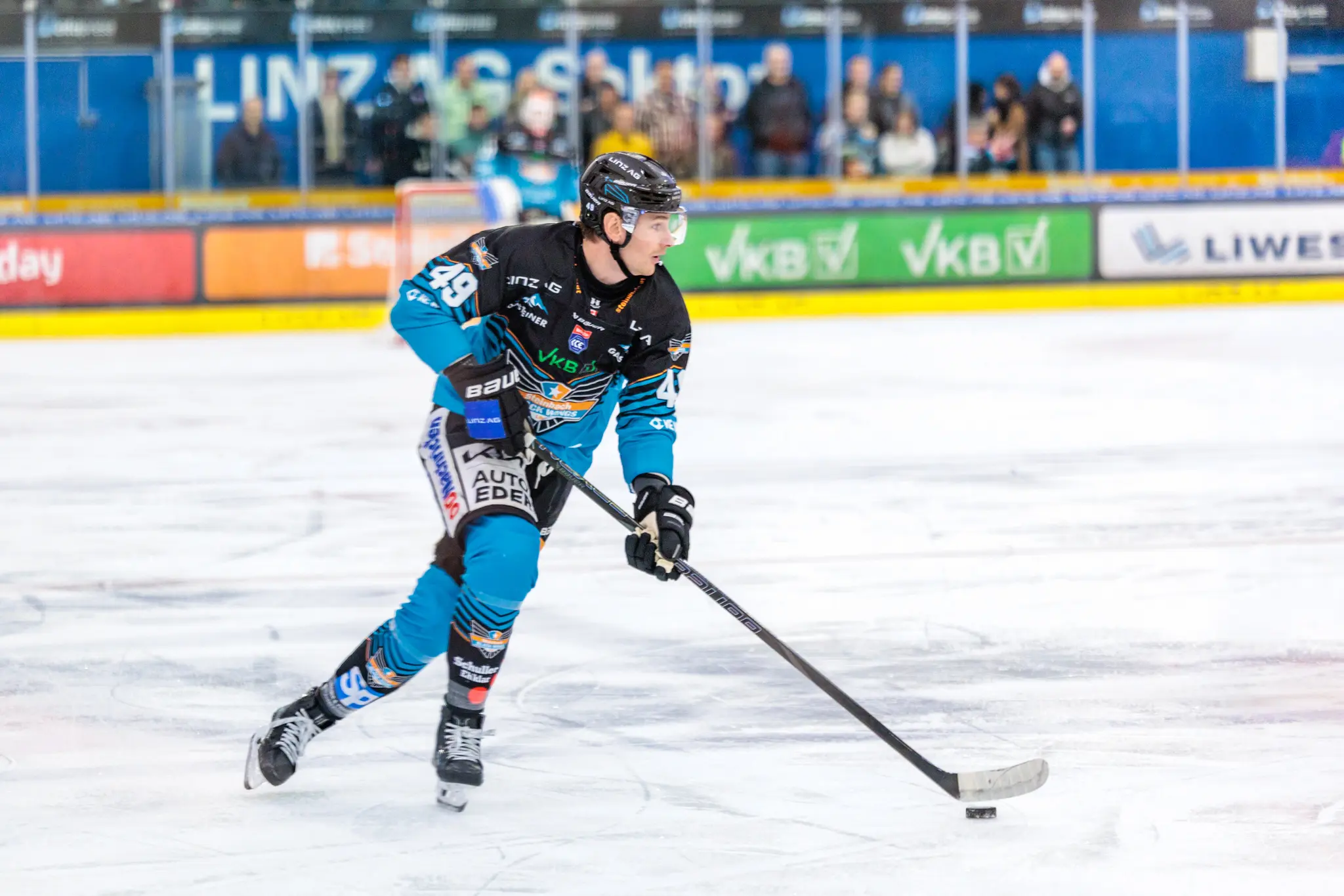 Der Eishockeyspieler Graham Knott von den Black Wings Linz mit der Nummer 49 führt den Puck in voller Aktion während eines Spiels über das Eis