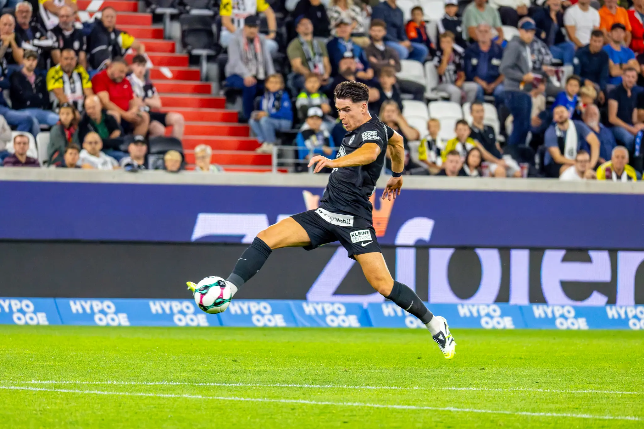 Ein Fußballspieler von Sturm Graz kontrolliert konzentriert einen Fußball auf dem grünen Spielfeld während eines Bundesligaspiels