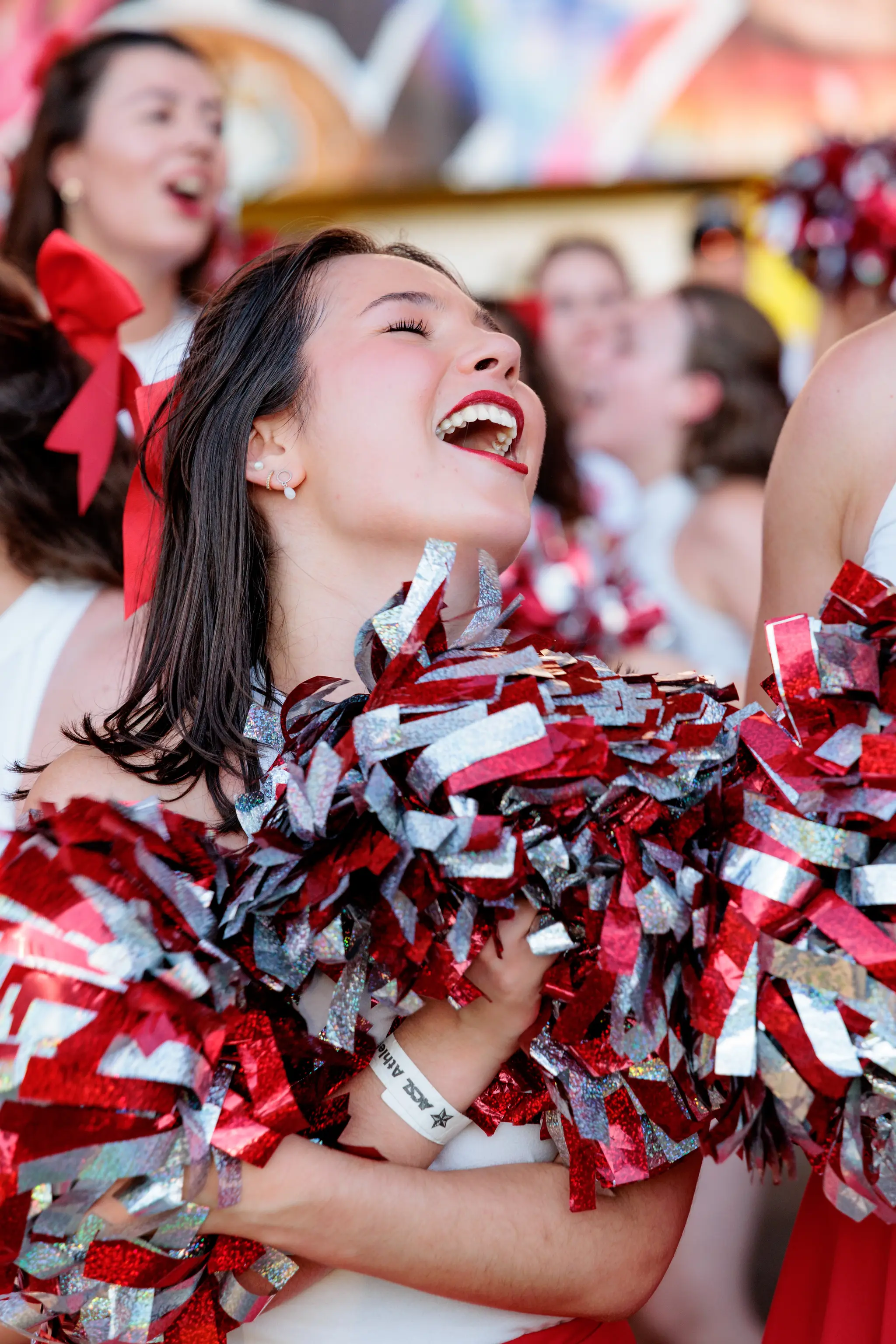 Eine strahlend lachende Cheerleaderin mit leuchtend roten und silbernen Pompons feiert ausgelassen bei einer ACSL-Sportveranstaltung