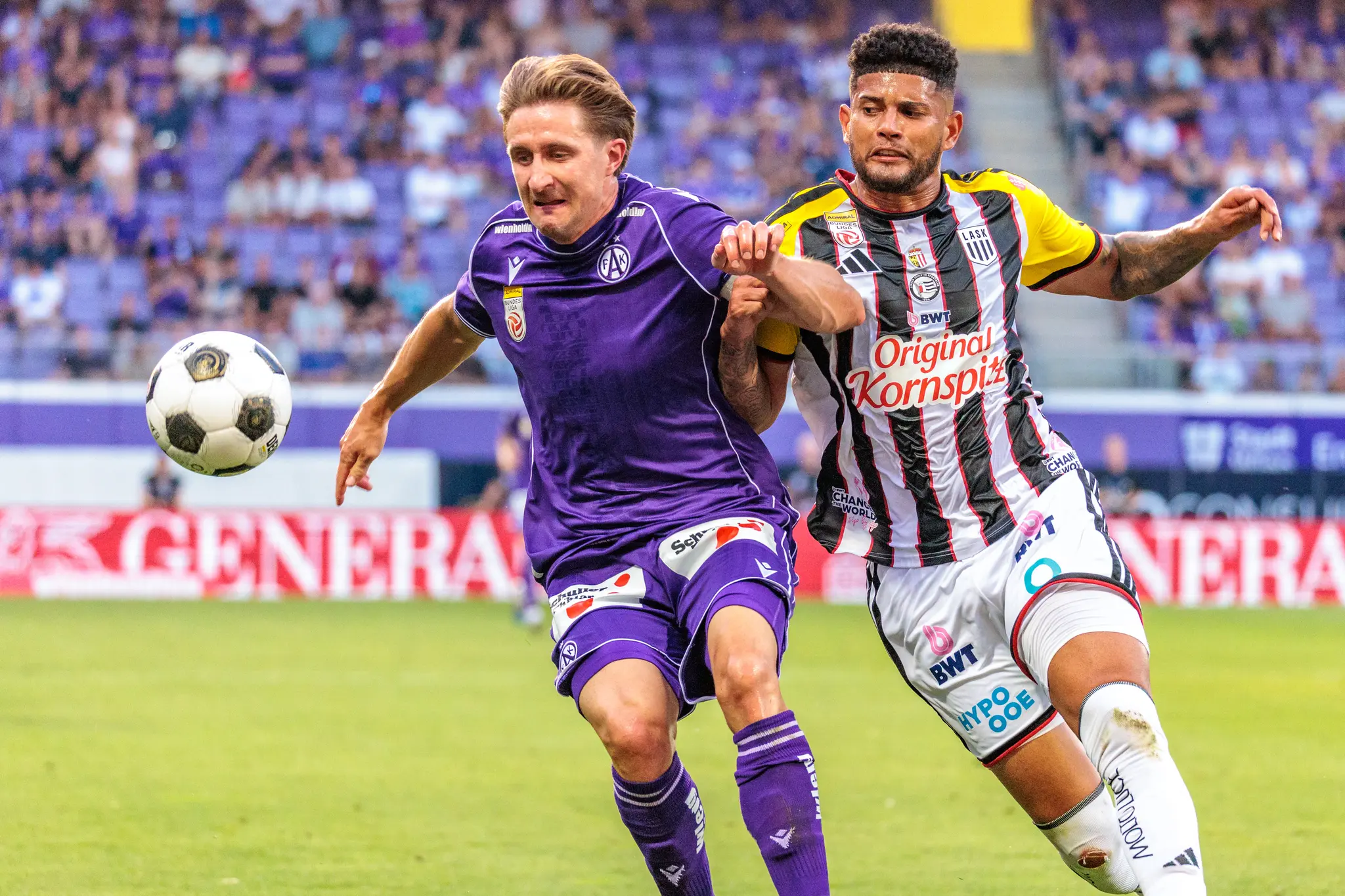 Austria- und LASK-Spieler sprinten gleichzeitig zum fliegenden Ball, beide heben die Arme zum Abfangen