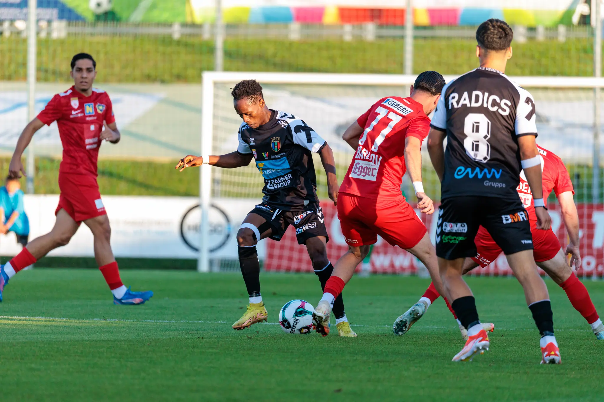 Intensiver Zweikampf um den Ball im Mittelfeld zwischen Spielern der SPG HOGO Wels in schwarzen Trikots und des SKN St. Pölten in roten Dressen während einer ÖFB Cup Partie