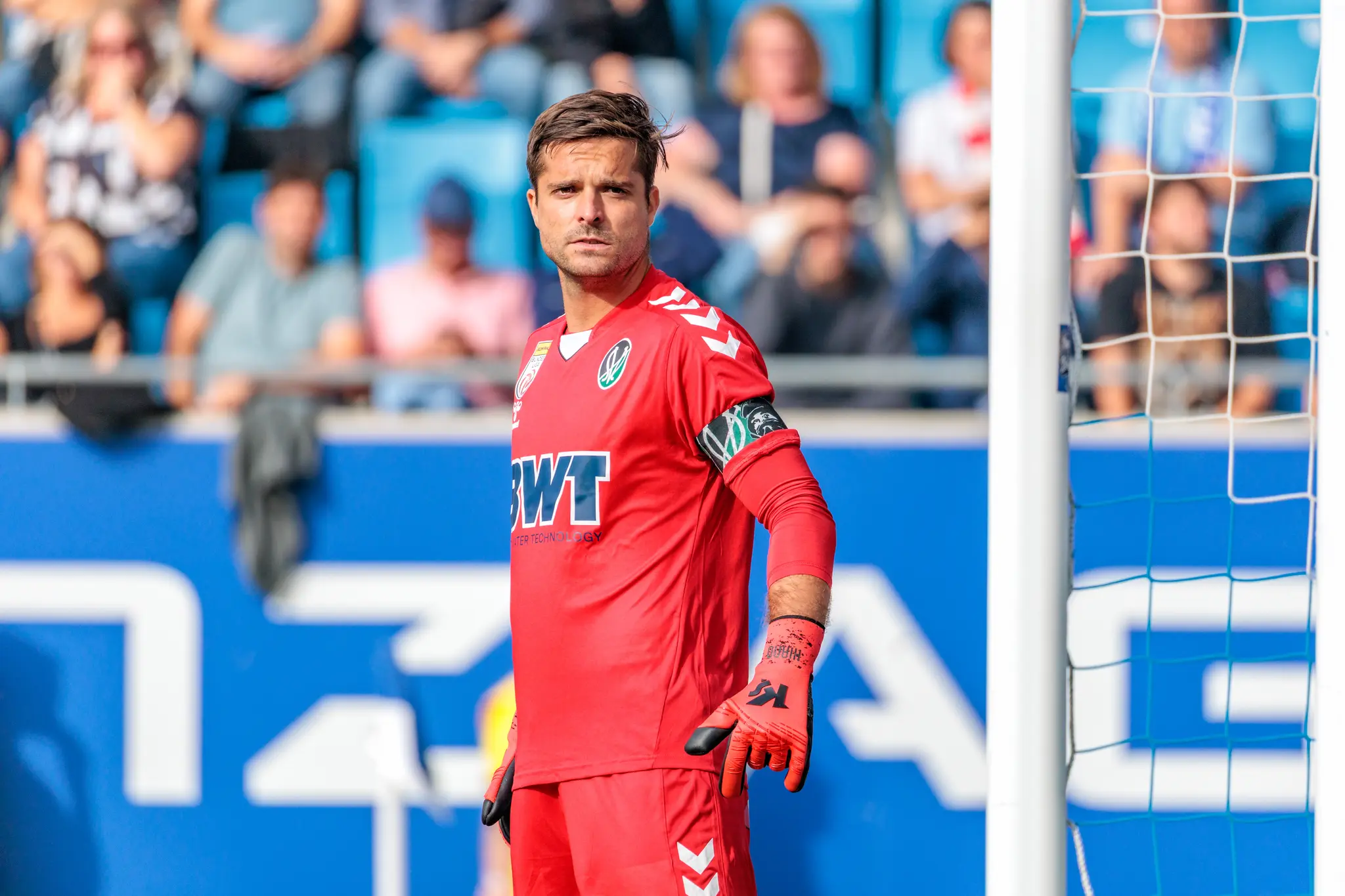 Der Torhüter des SV Ried blickt in seiner roten Spielertracht konzentriert in die Kamera während des Bundesliga-Derbys gegen Blau-Weiß Linz