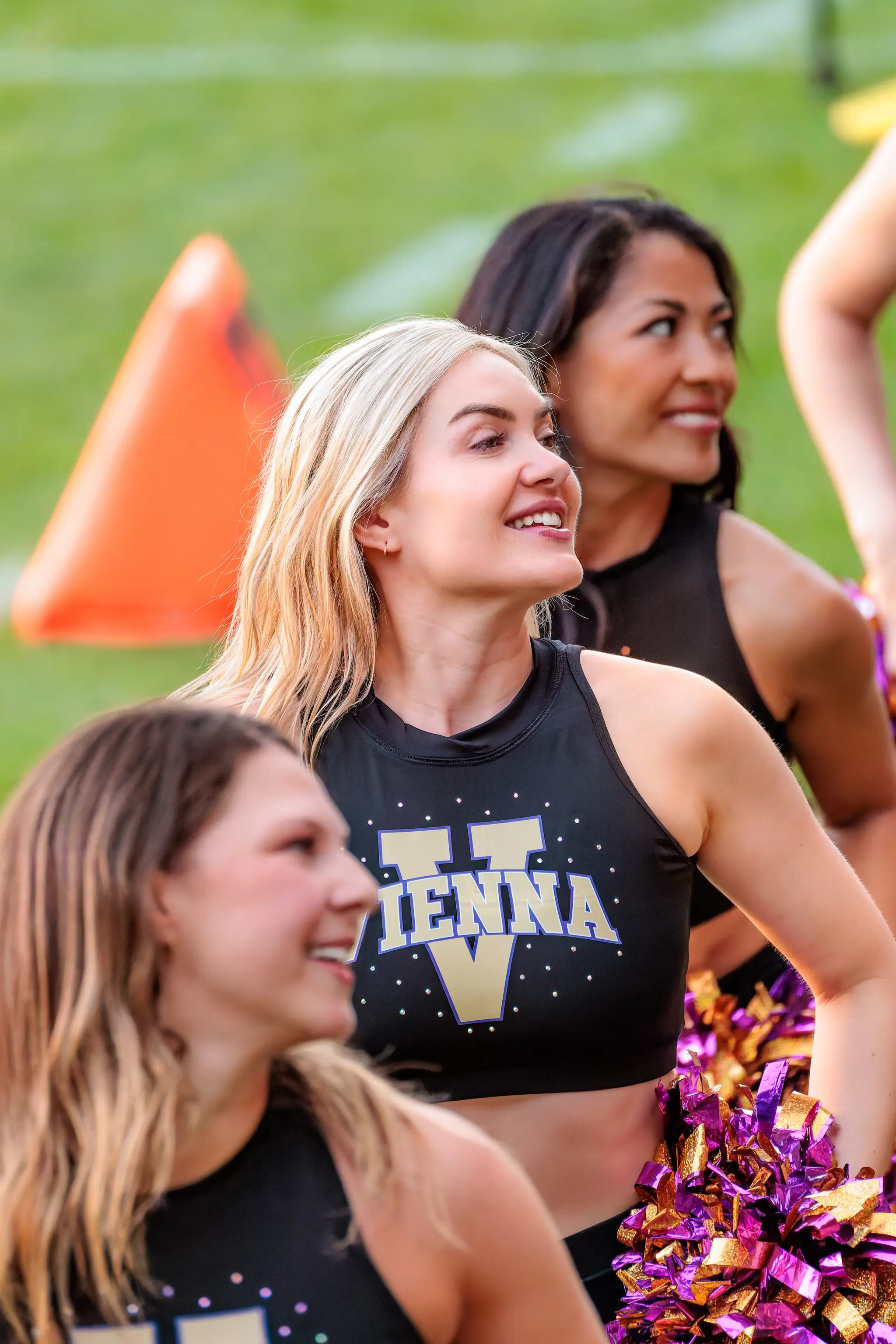Cheerleaderin des Spirit Squad steht aufrecht, lächelt, den Kopf nach oben rechts gedreht, Pompons auf Hüfthöhe.
