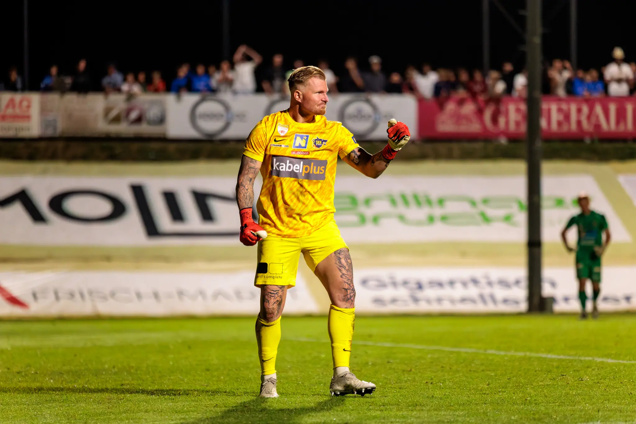Der tätowierte Torwart von St. Pöten im gelben Trikot jubelt auf dem Feld bei einem ÖFB-Cup-Spiel unter Flutlicht