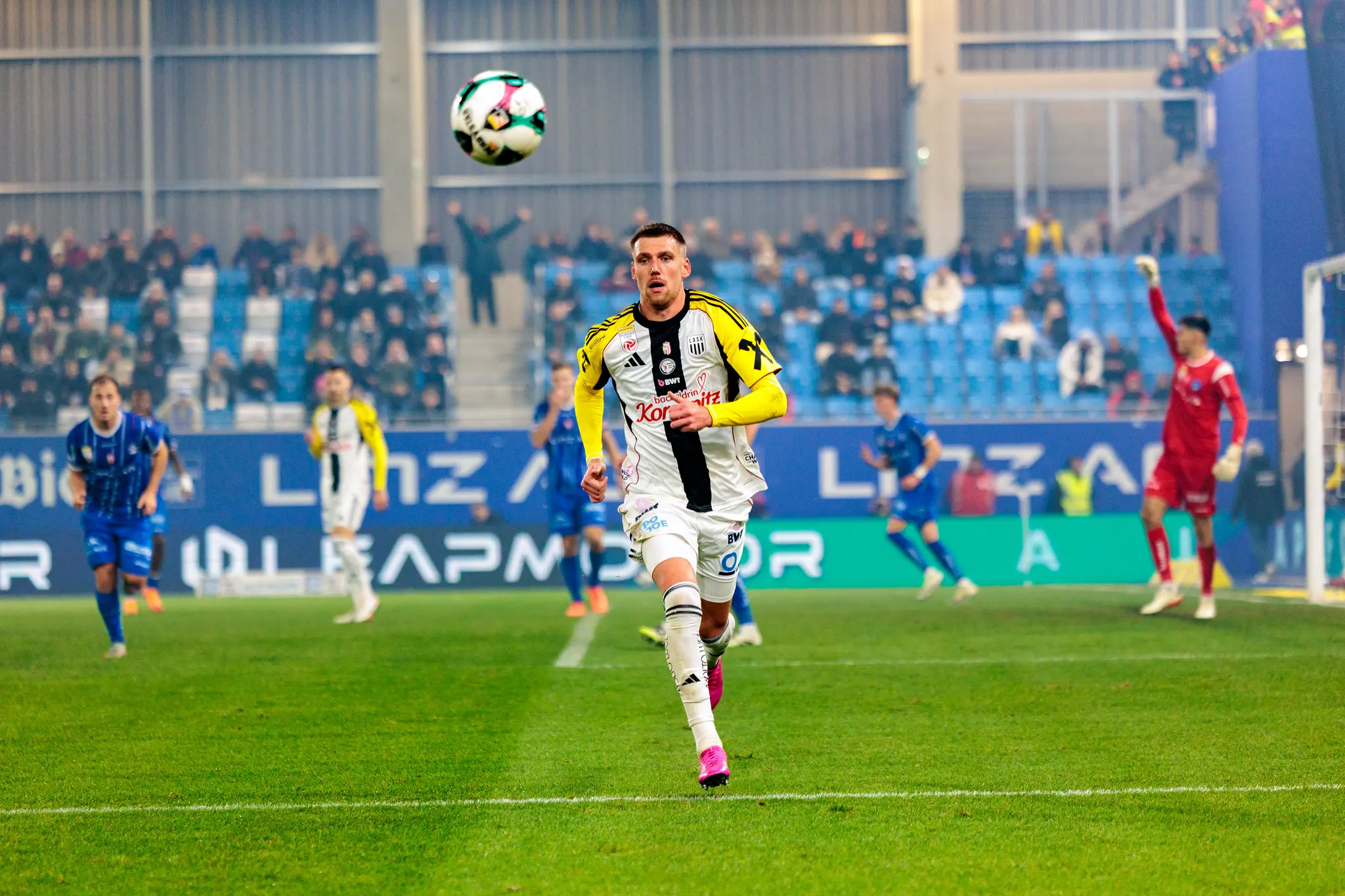 Der LASK-Spieler Florian Flecker in dynamischer Laufpose während des Linzer Derbys, der Fußball schwebt über ihm in der Luft