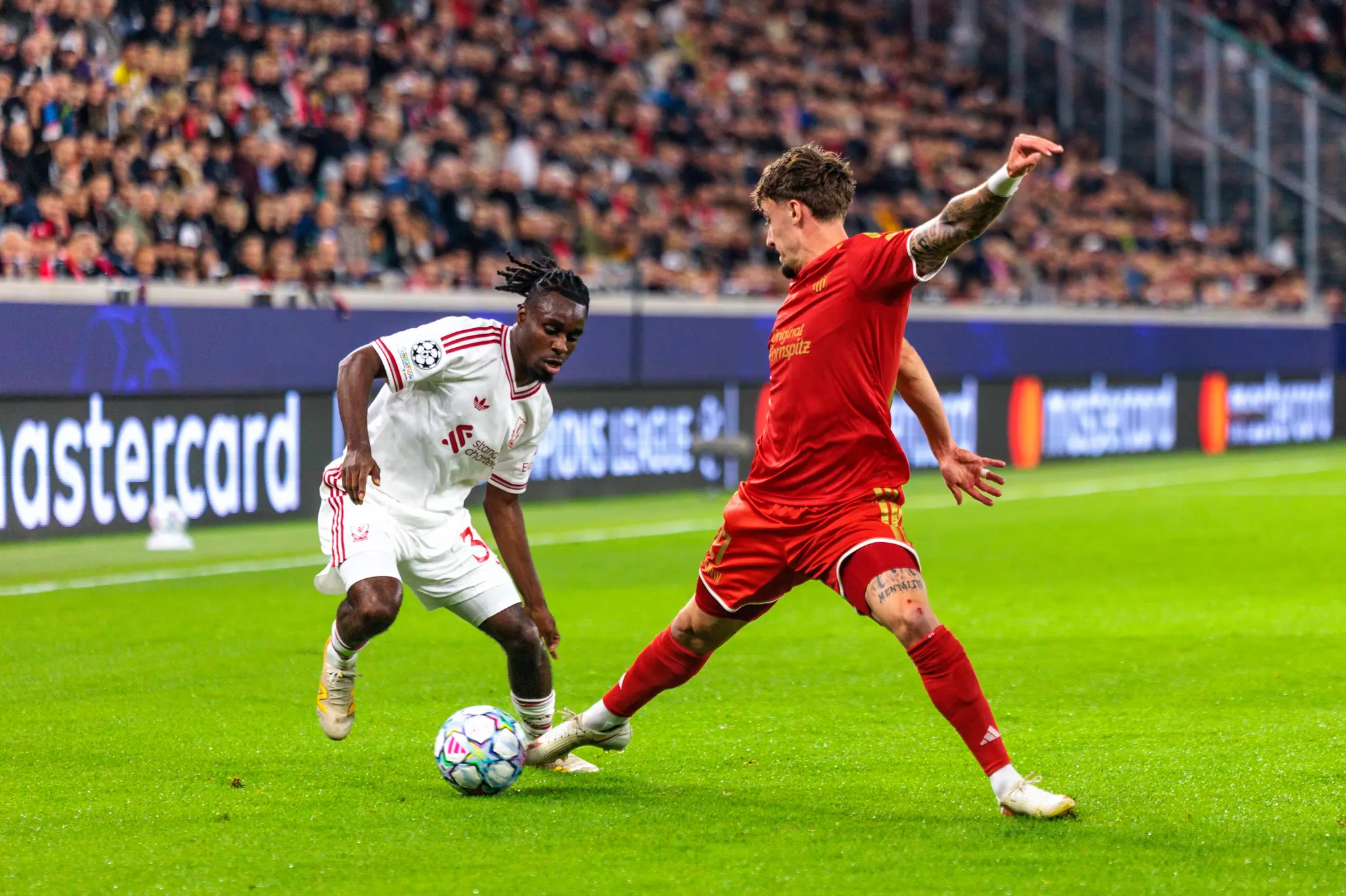 Ein Liverpooler Spieler in Weiß und ein LASK-Spieler in Rot sprinten beide zu dem Ball, der zwischen ihnen auf dem Rasen liegt.