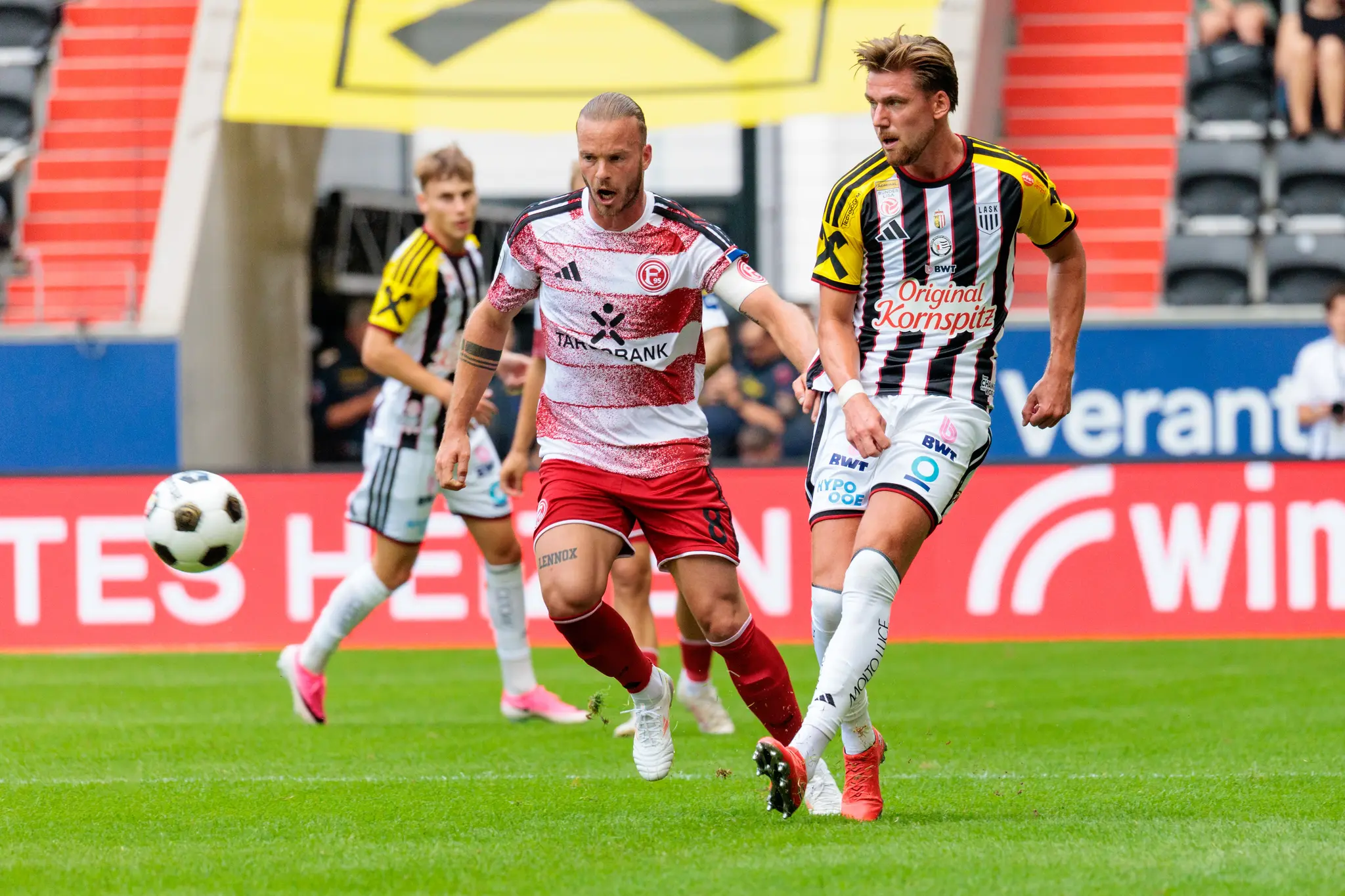 Duell zwischen einem Düsseldorfer Spieler und einem LASK-Spieler um den Ball im Mittelfeld, beide kämpfen intensiv um das Leder.