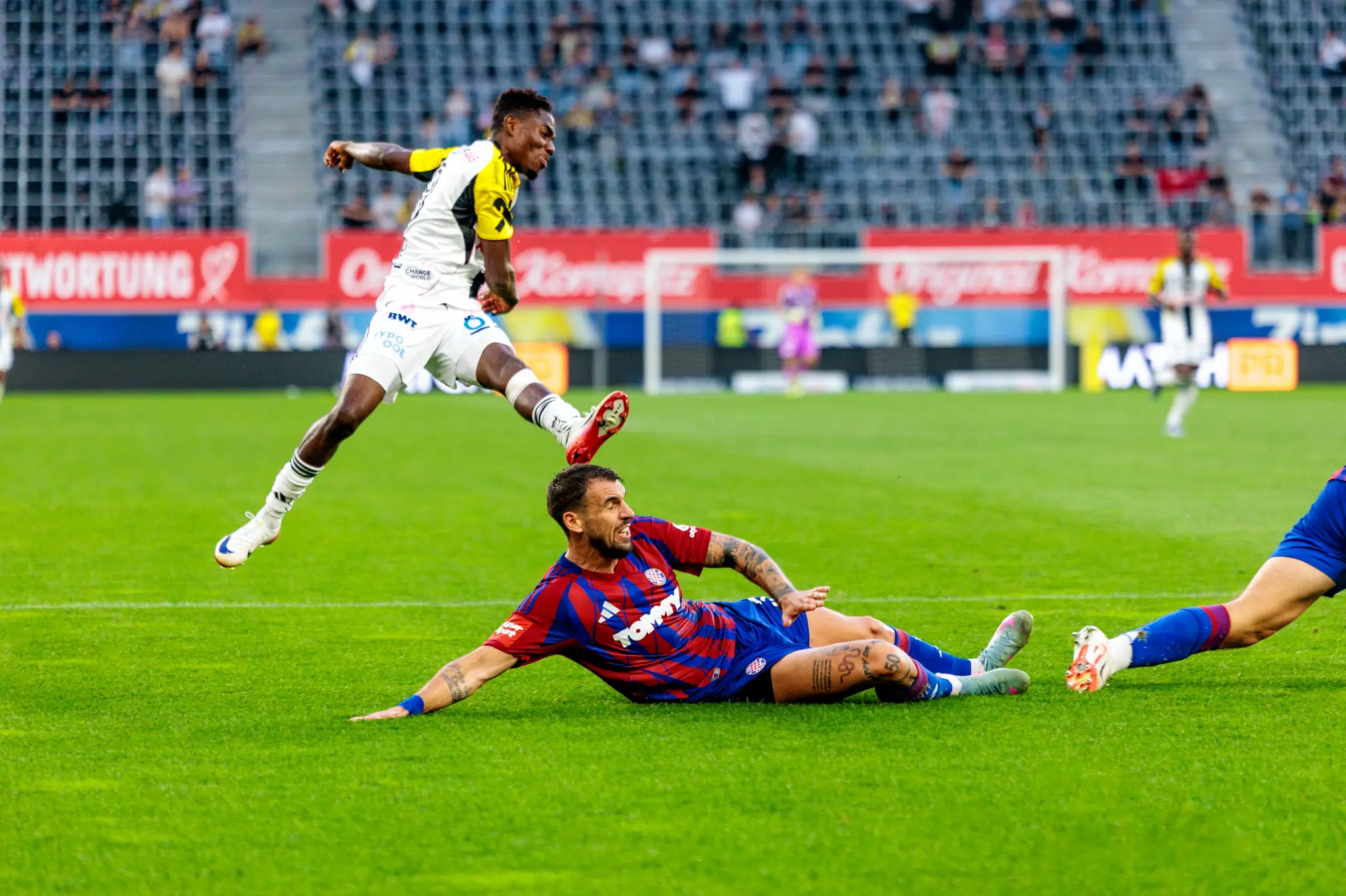 Ein Fußballspieler des LASK springt nach einem Schuss über einen über den Boden rutschenden Gegenspieler 