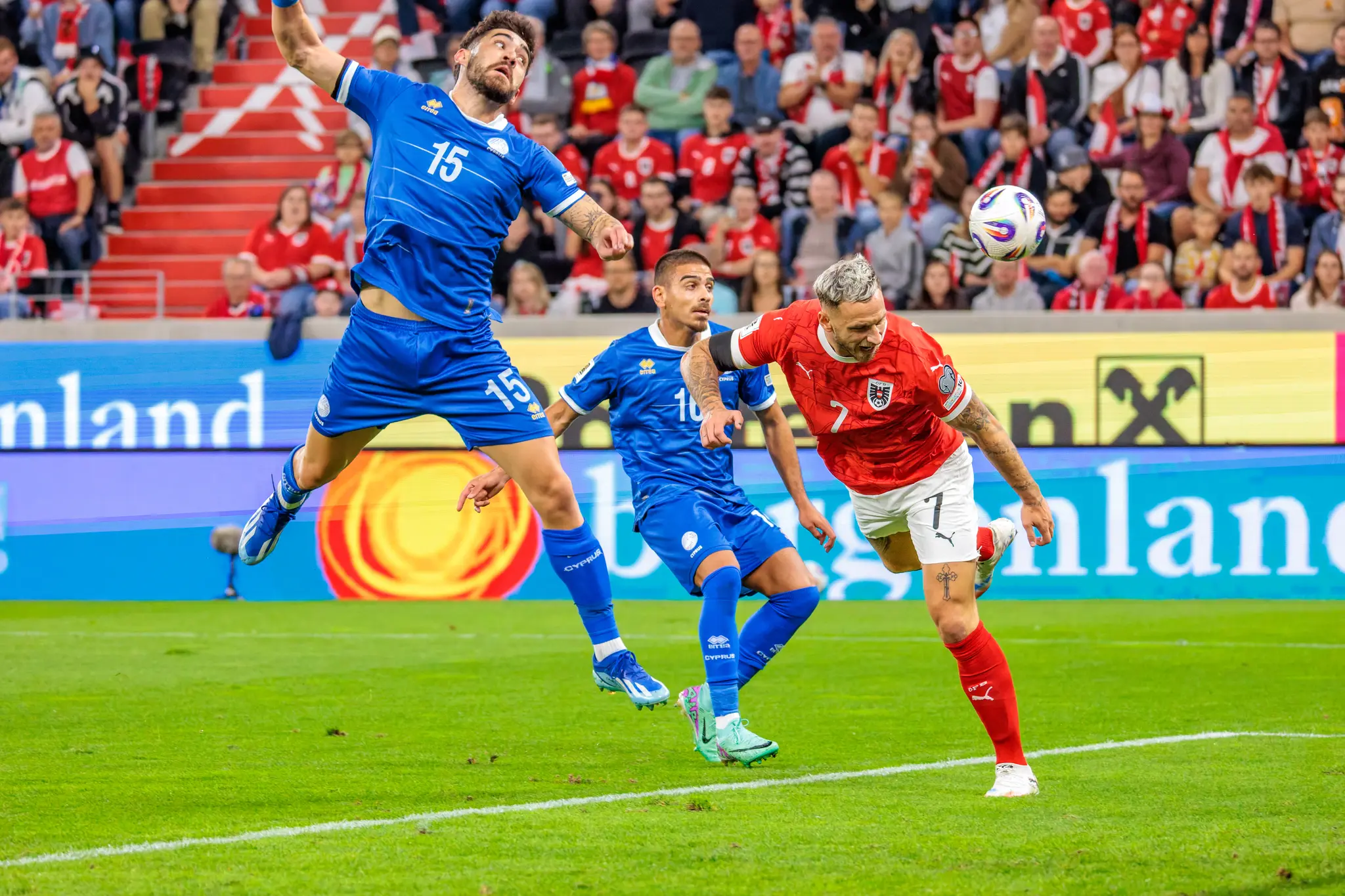 Marko Arnautović im roten Trikot von Österreich und Christos Shelis im blauen Trikot von Zypern springen in einem Kopfballduell um den Fußball vor vollen Zuschauerrängen