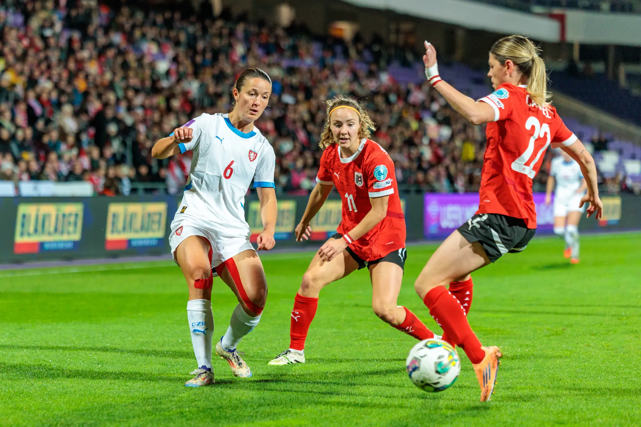Eine österreichische Nationalspielerin im roten Trikot dribbelt mit dem Ball und wird in einem intensiven Zweikampf von einer tschechischen Spielerin attackiert