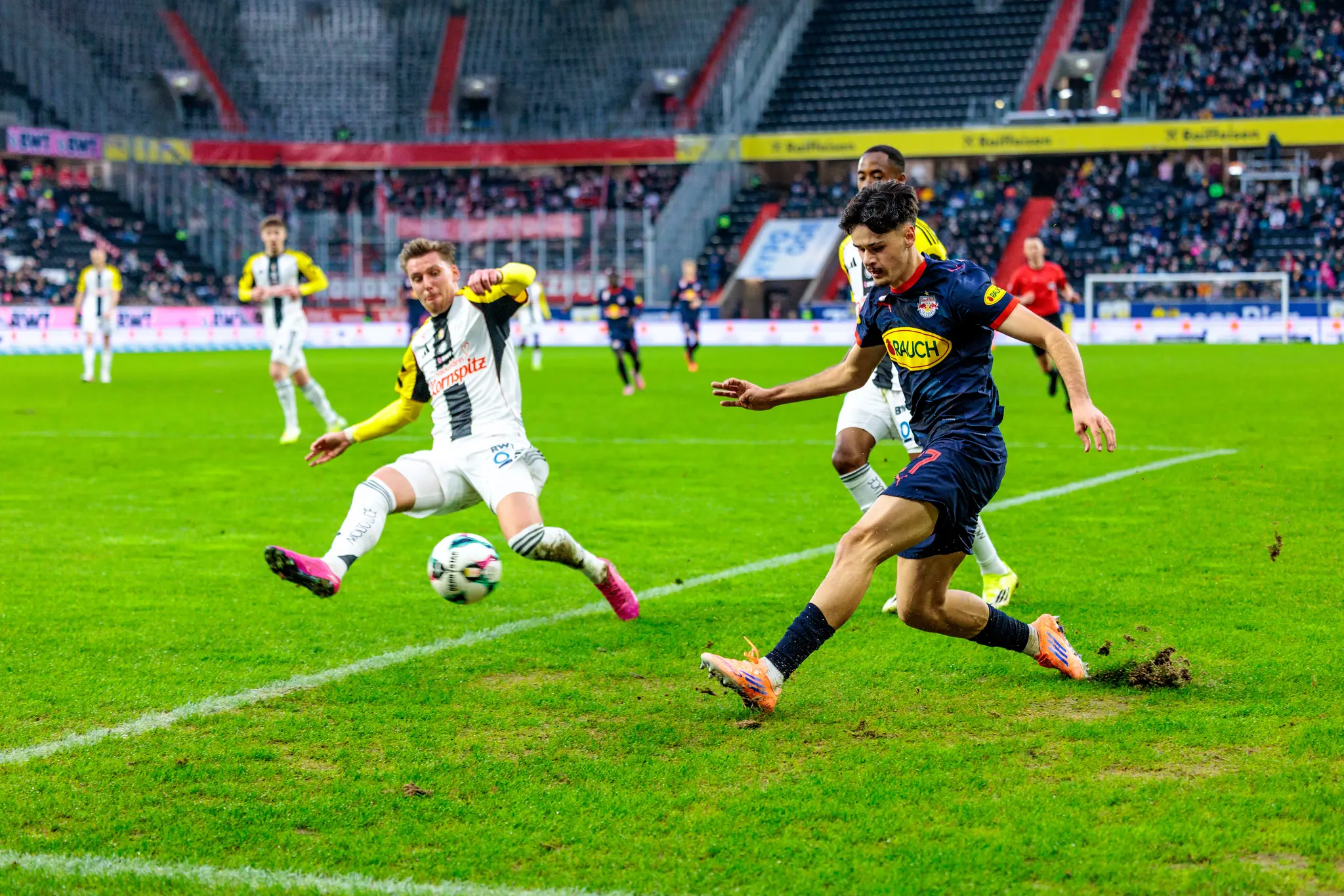 Ein Spieler von Red Bull Salzburg behauptet im intensiven Zweikampf den Ball gegen einen grätschenden Verteidiger des LASK während der Admiral Bundesliga