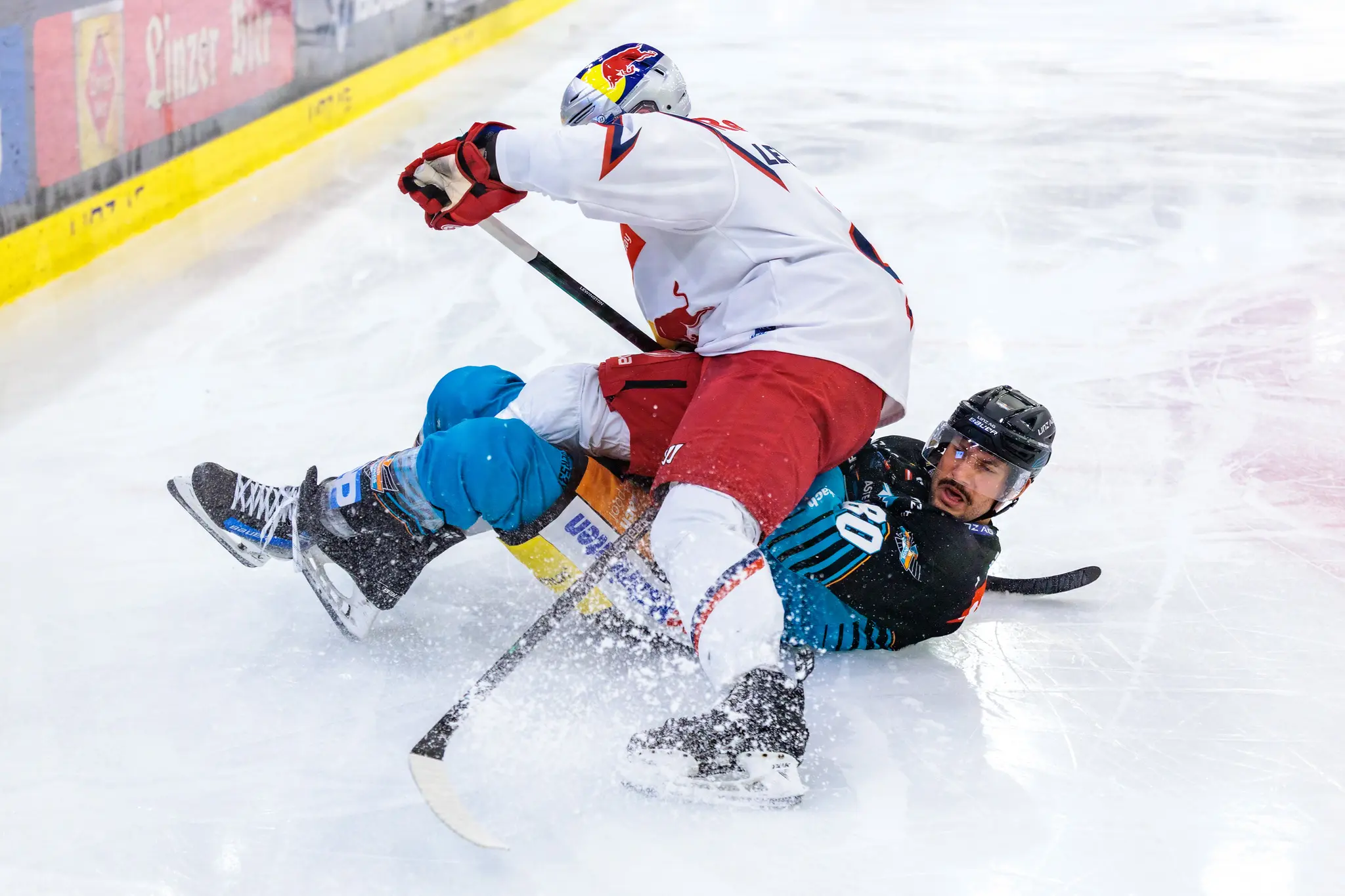 Julian Pusnik von den Steinbach Black Wings Linz wird im intensiven Eishockey-Zweikampf von Tyler Lewington vom EC Red Bull Salzburg zu Boden gerungen